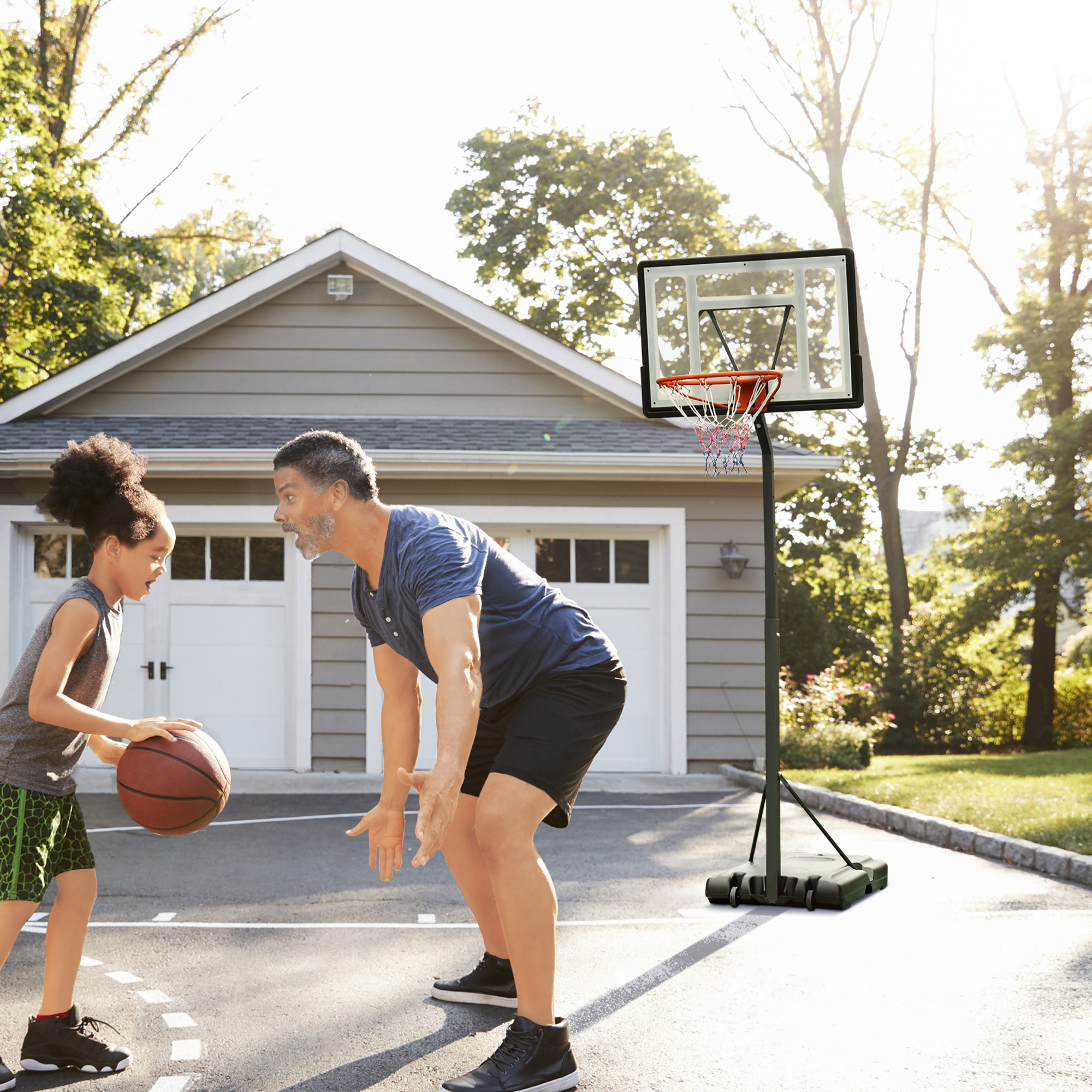 Un hombre y un niño juegan al baloncesto en una entrada. Hay un aro de baloncesto en el fondo. Una casa también está en el fondo.