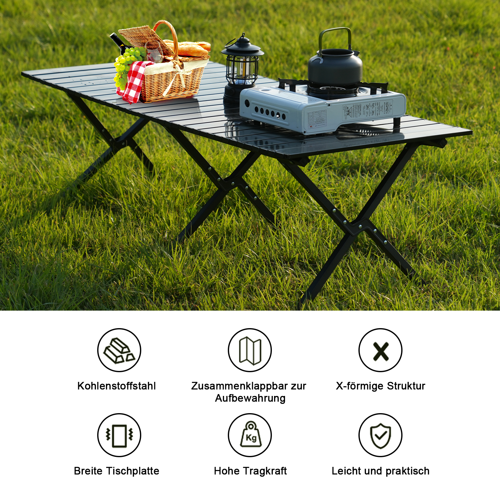 Ein schwarzer Klapptisch auf Gras mit Picknickkorb, Lampe, Gasherd und Wasserkocher. Der Tisch ist gedeckt.