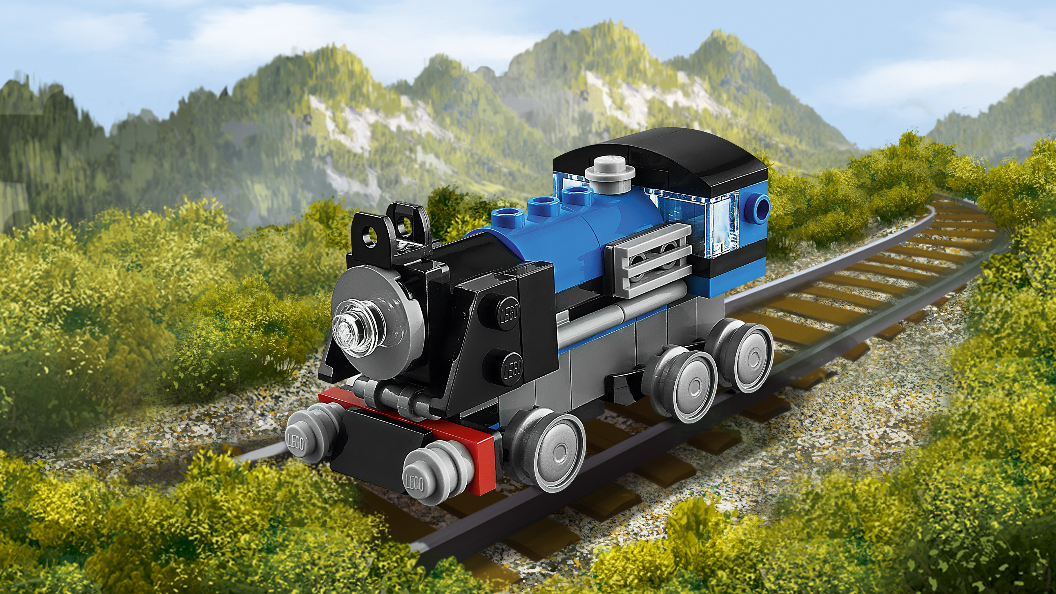 Un treno Lego blu, nero e grigio è su un binario, montagne e vegetazione sullo sfondo, cielo blu. Il treno ha sei ruote.