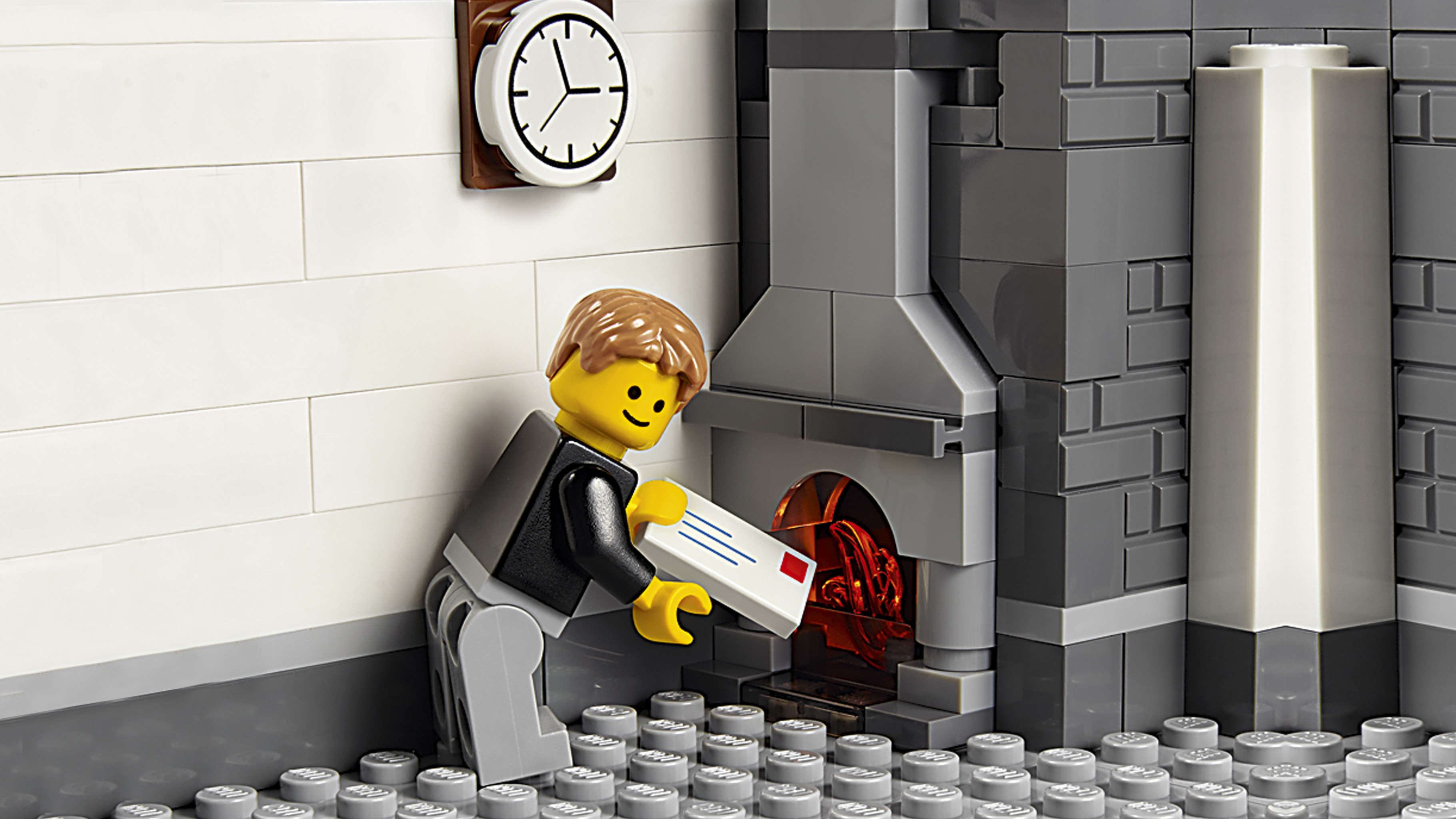 Figurka Lego wkłada list do kominka Lego. Zegar wisi na ścianie. Scena wykonana jest z klocków Lego.