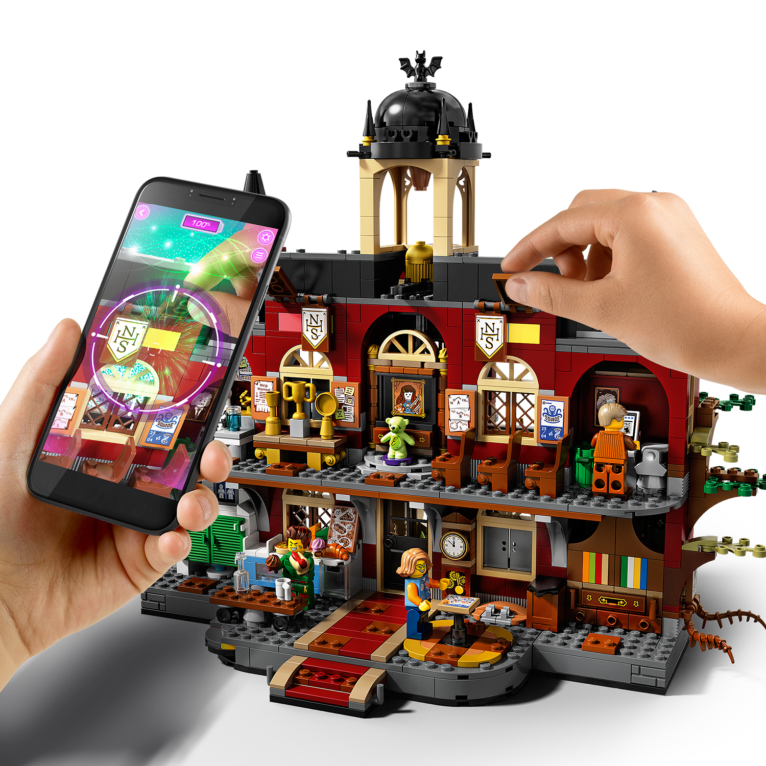 Ręce wchodzące w interakcję z zestawem Lego, jeden trzyma telefon z nakładką rozszerzonej rzeczywistości, drugi dodaje element.
