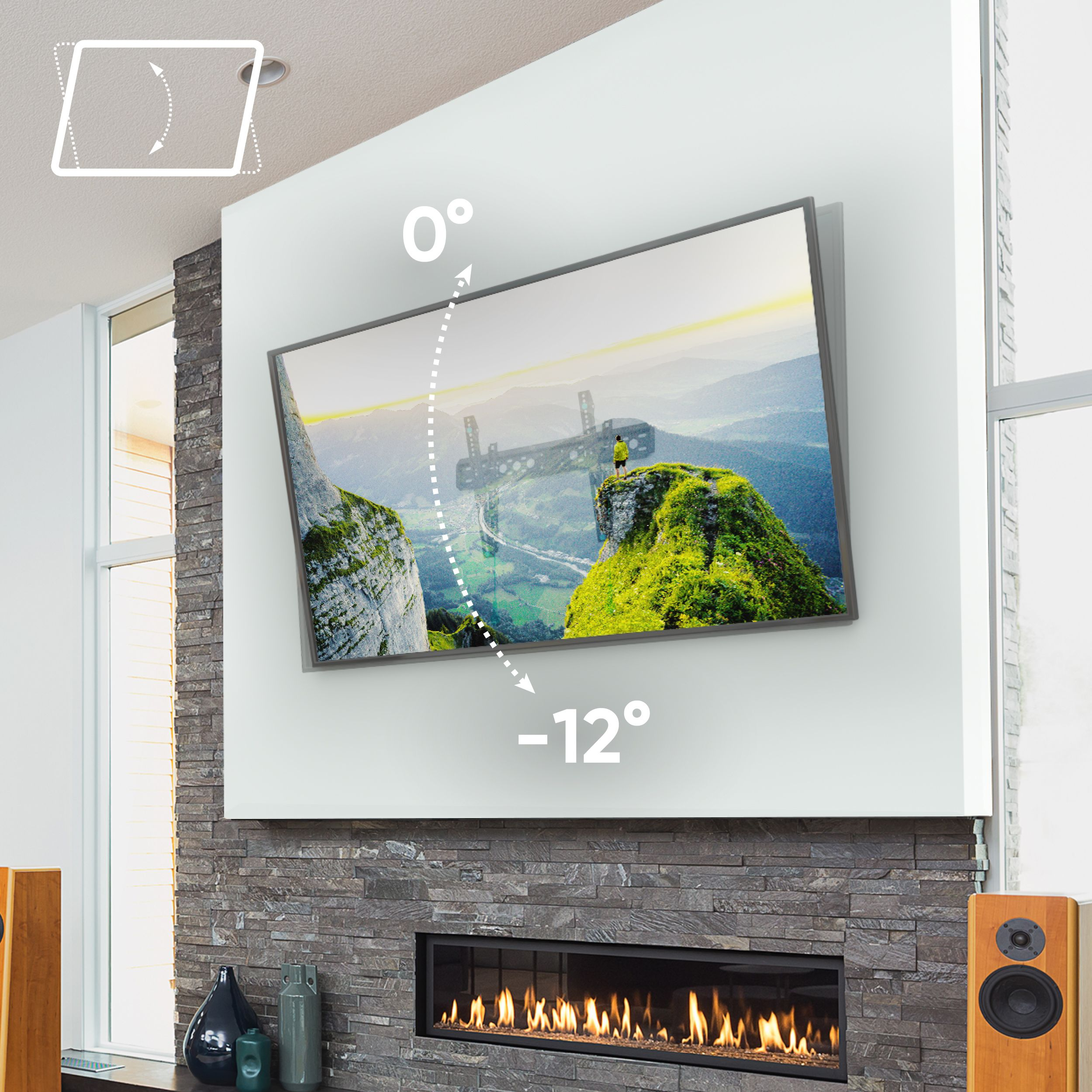 Telewizor pochylony na ścianie, kominek, głośniki i okna. Telewizor pokazuje górski krajobraz. Ściana jest z szarego kamienia.