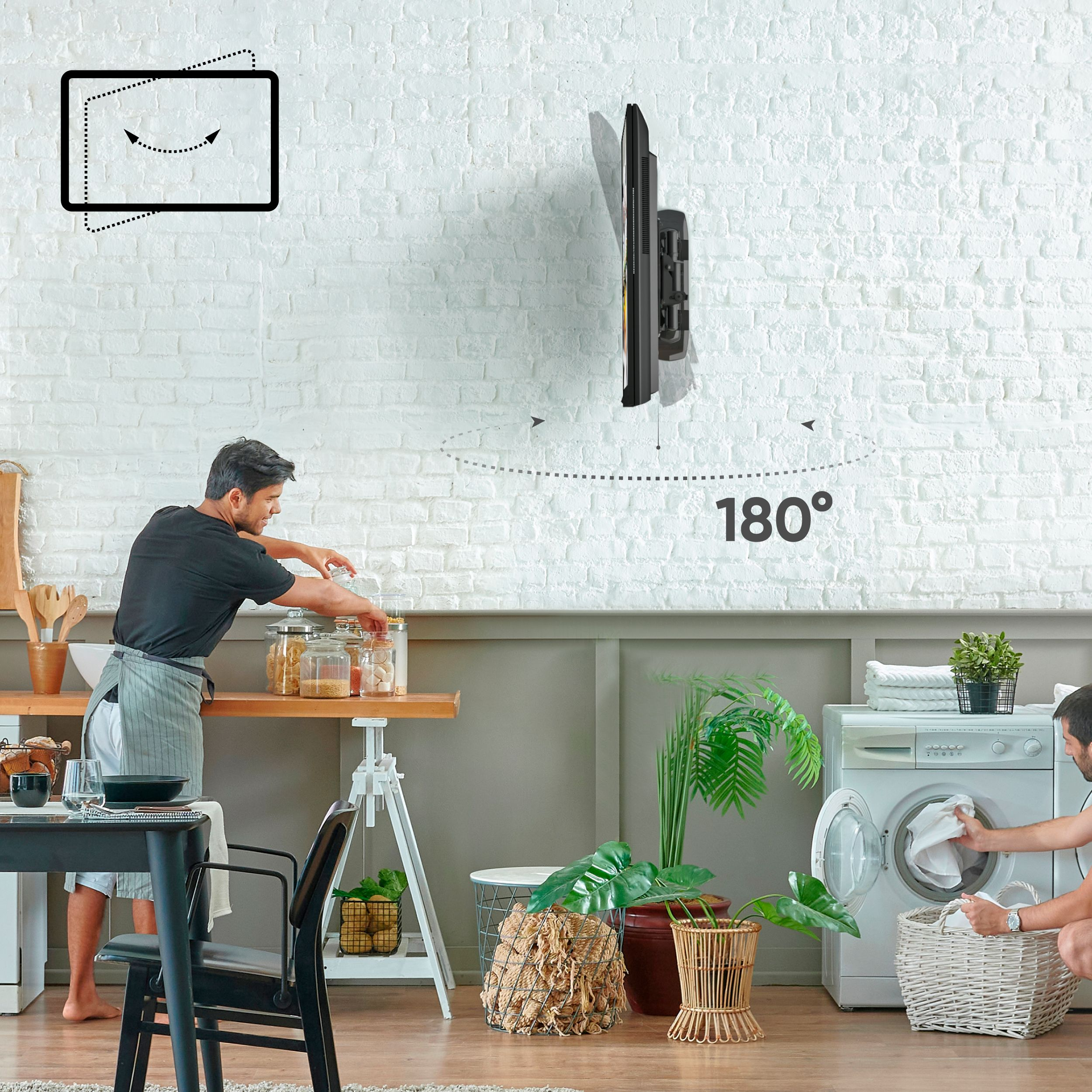 Mężczyzna w kuchni przygotowuje jedzenie, a drugi ładuje pralkę. Telewizor jest zamontowany na białej ceglanej ścianie.