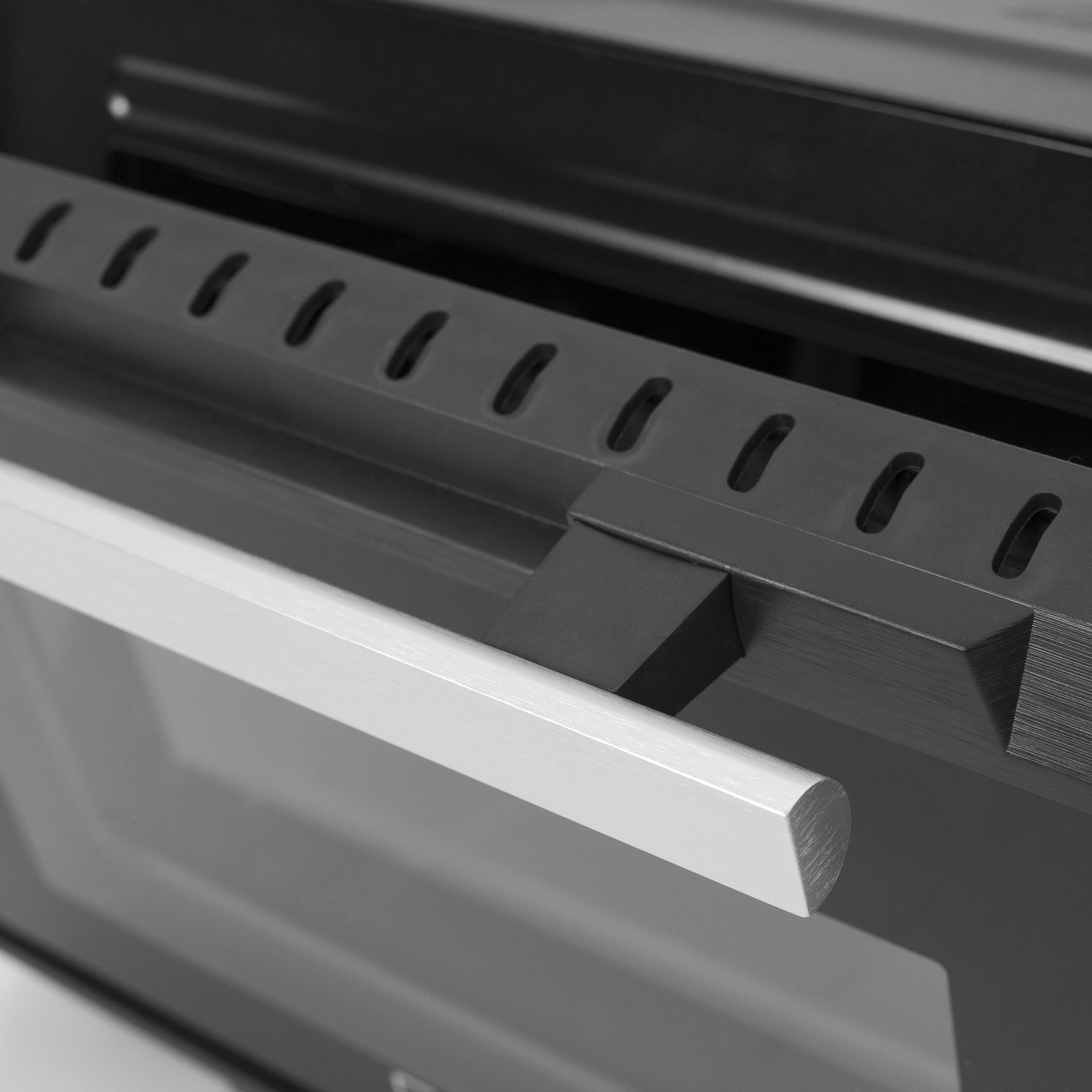 Primo piano dell'interno di un forno. È visibile una griglia metallica con fori, insieme a una maniglia bianca. La scena è in scala di grigi.