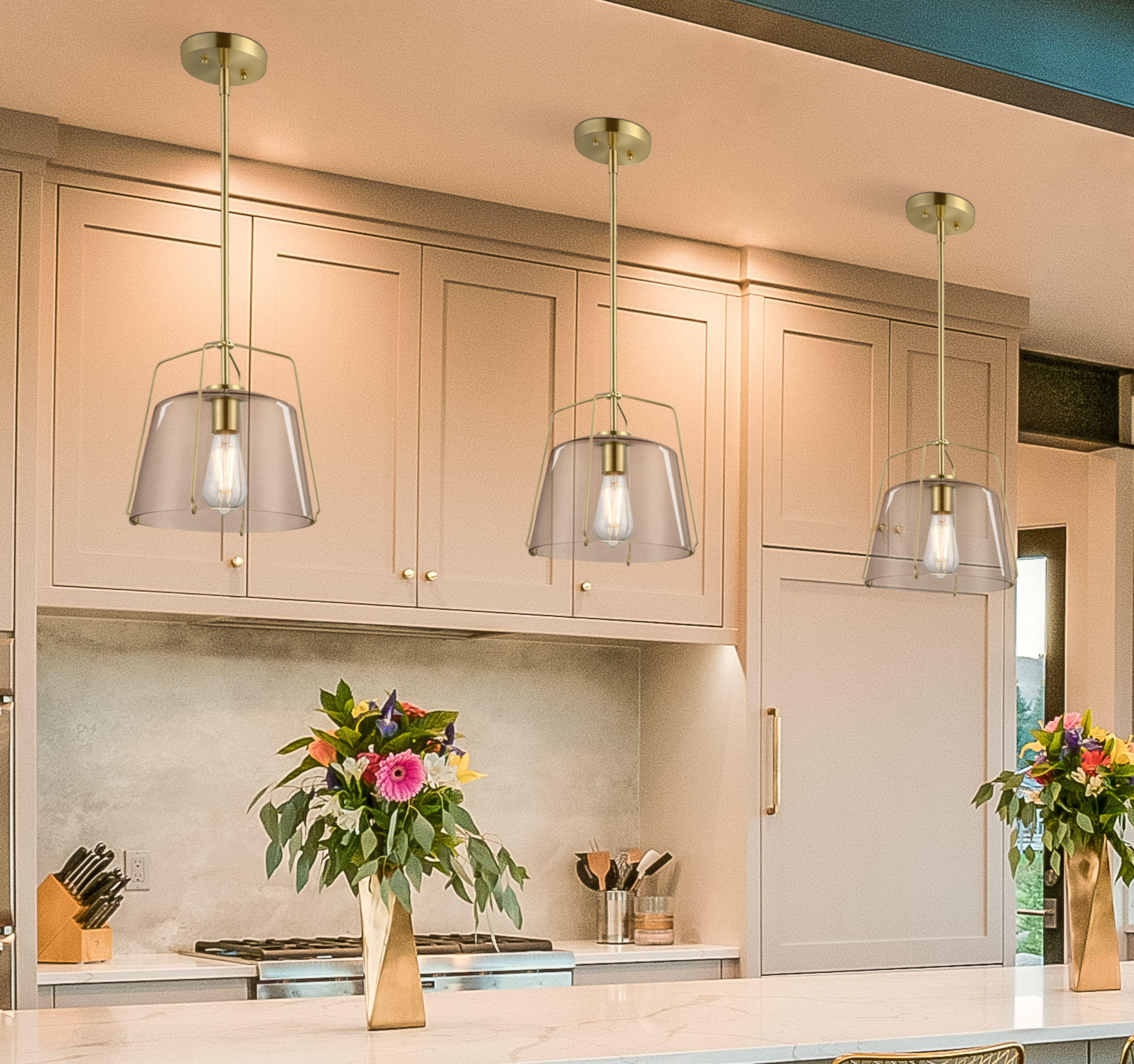 Küche mit drei Hängelampen, Blumen in Vasen und Schränken. Die Lampen haben Glasschirme. Vorne ist eine Arbeitsplatte.