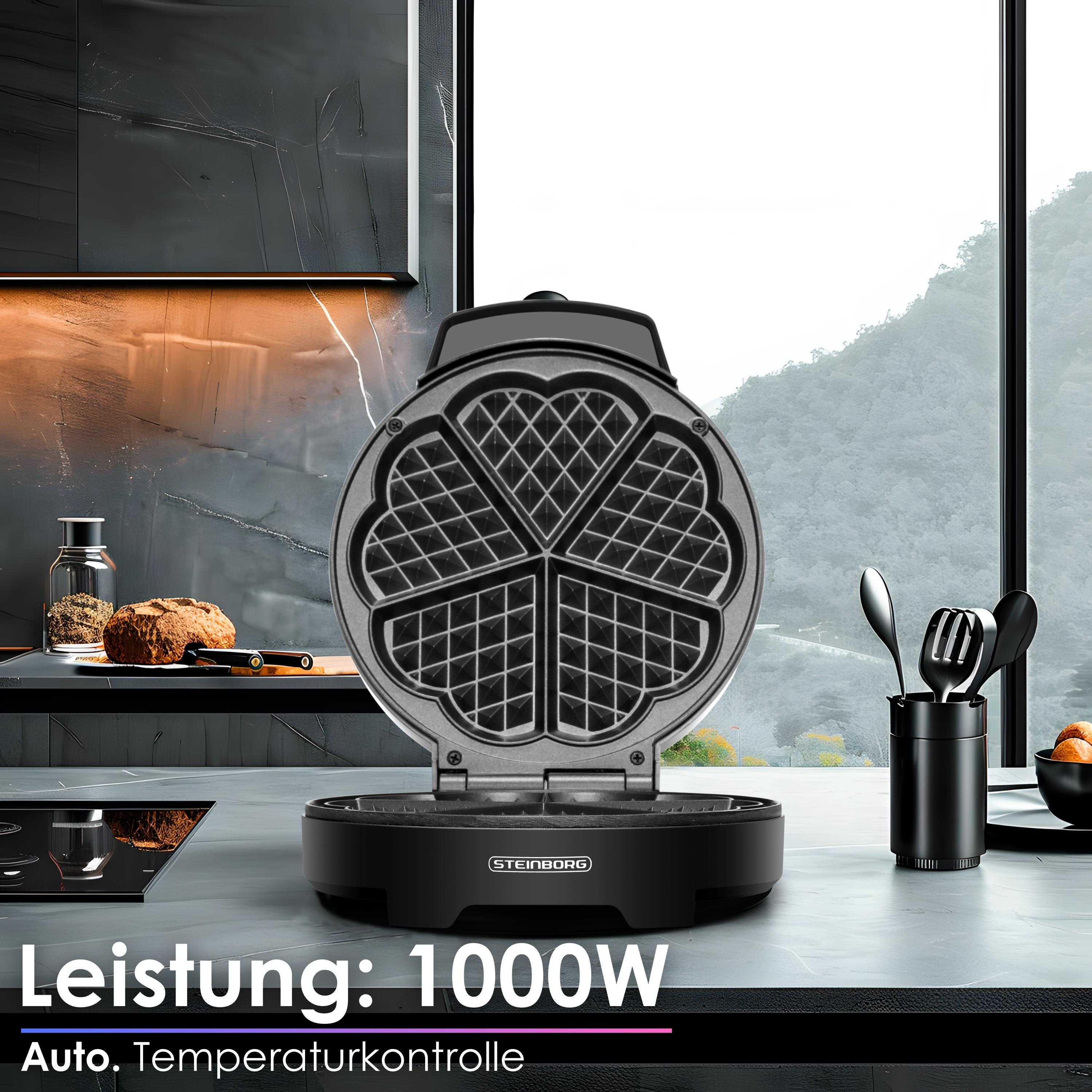 Waffeleisen mit herzförmigen Gittern auf einer Theke. Ein Fenster zeigt eine Berglandschaft. Utensilien und Brot sind daneben.