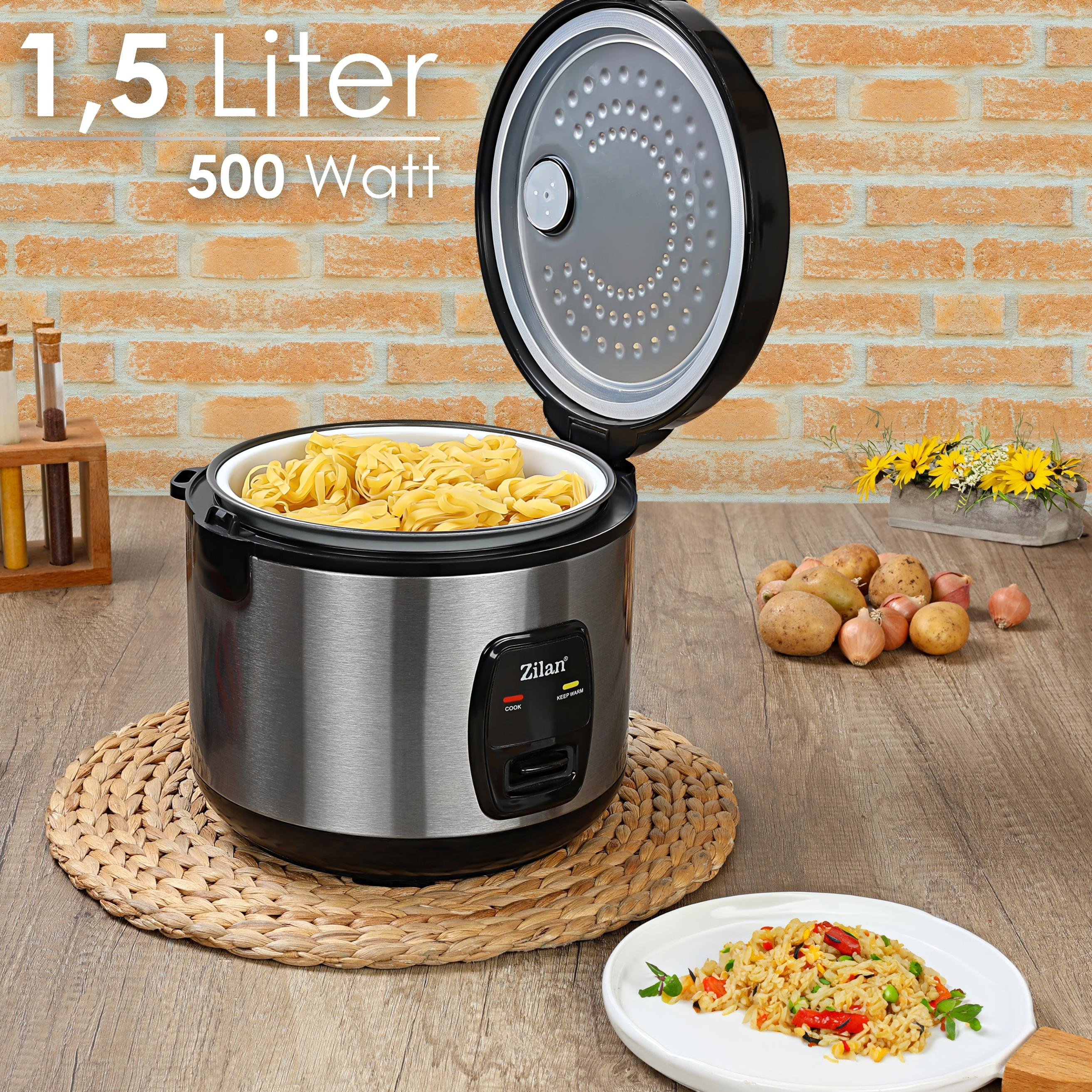 Reiskocher mit Pasta im Inneren, auf einer gewebten Matte. Zutaten und gekochter Reis sind daneben. Ziegelwandhintergrund.