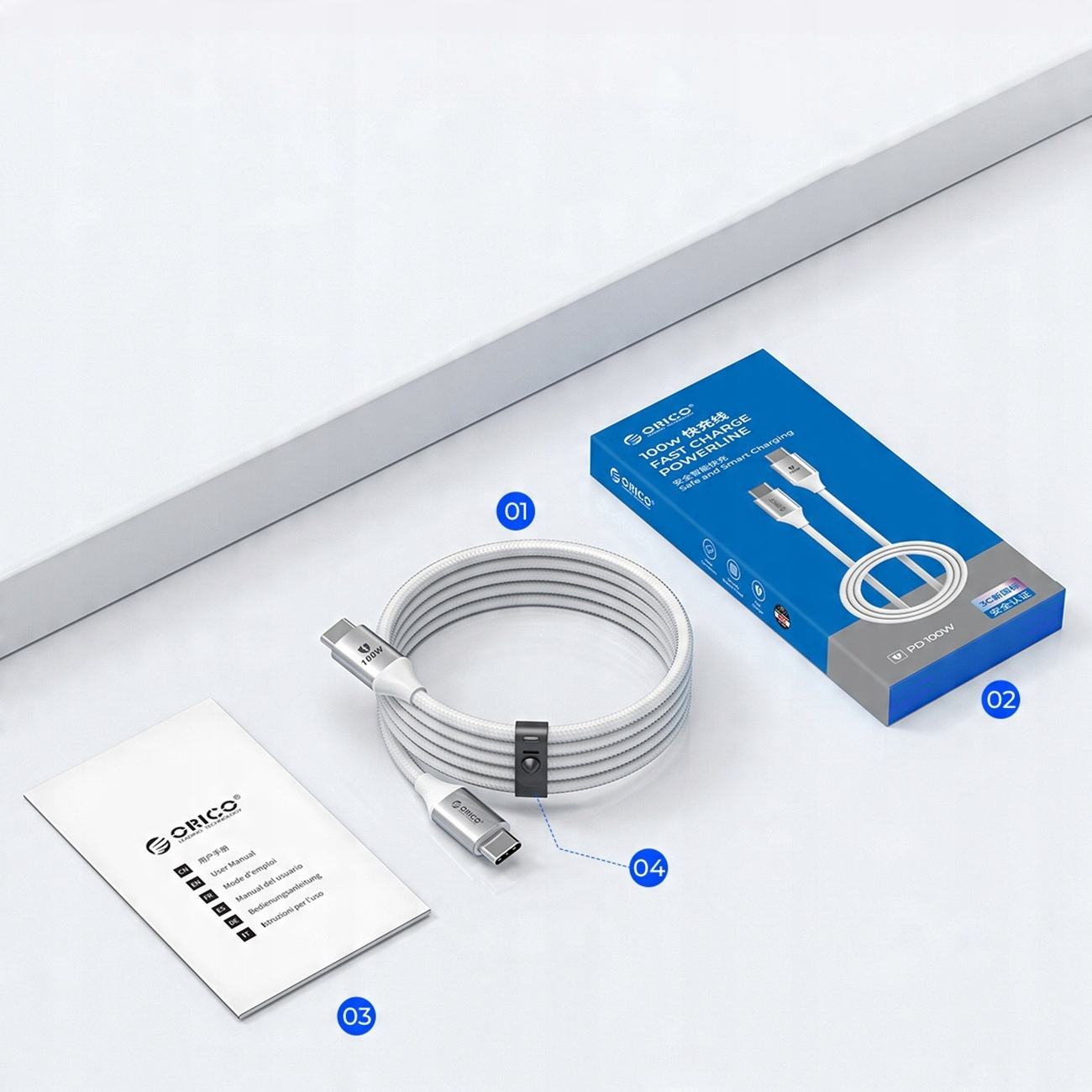 Ein aufgerolltes weißes Ladekabel mit schwarzem Clip, eine blaue Box und eine Bedienungsanleitung auf weißer Oberfläche.
