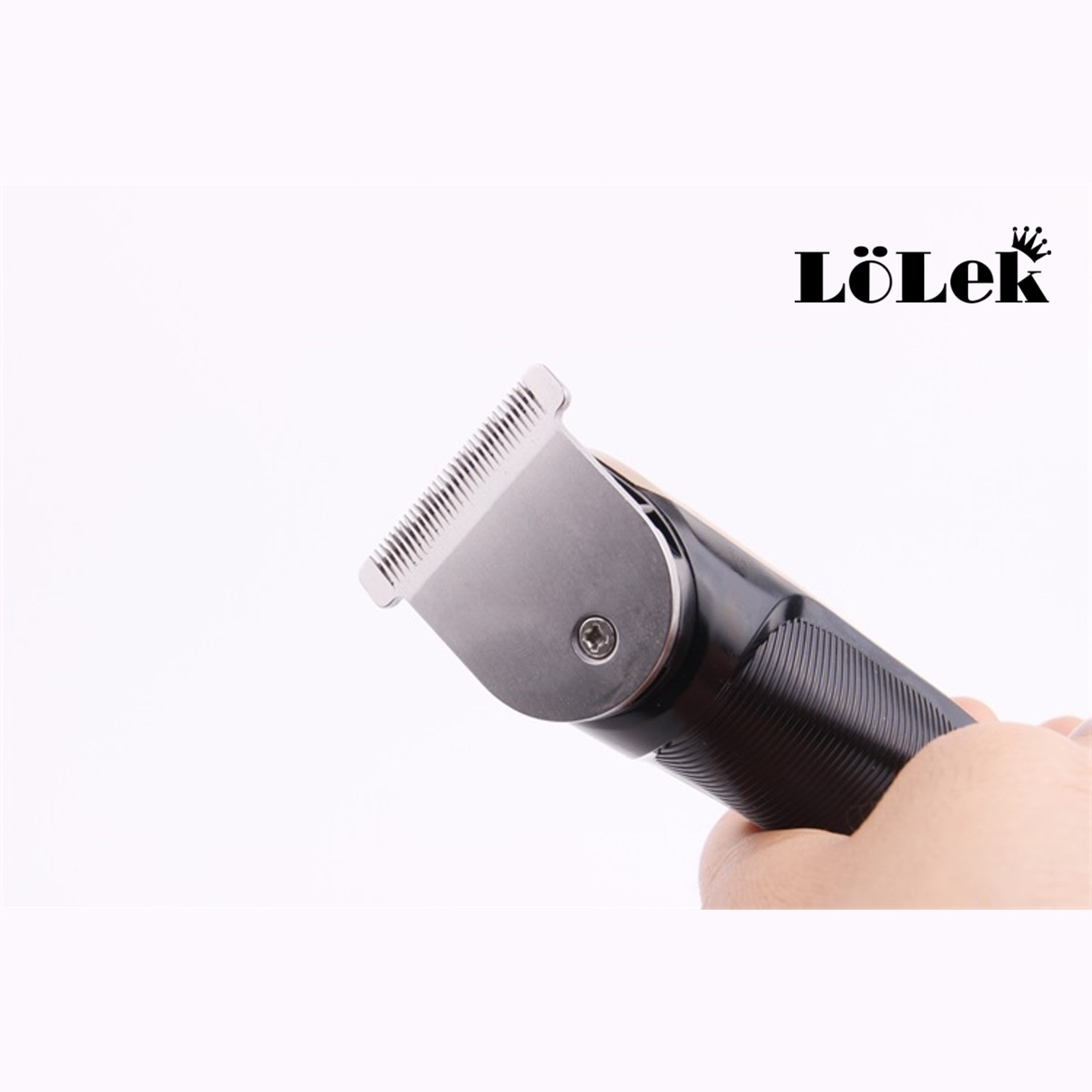 Primer plano de una cortadora de pelo negra y plateada sostenida por una mano contra un fondo blanco. La marca es LöleK.