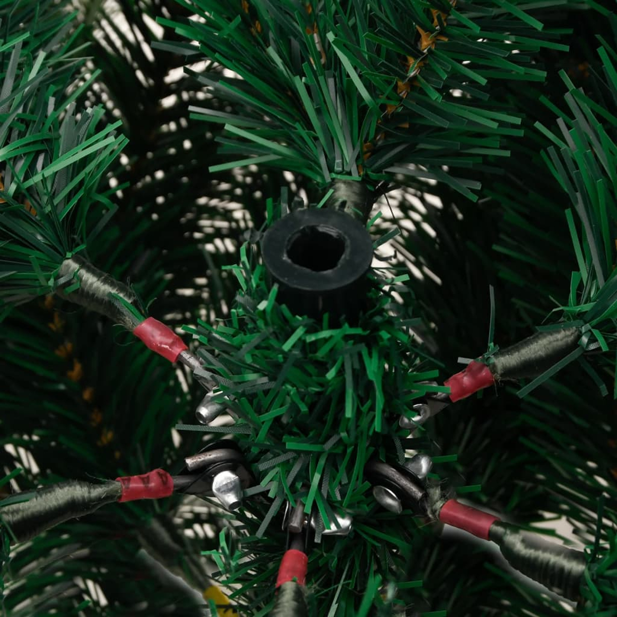 Nahaufnahme eines grünen künstlichen Weihnachtsbaumfußes. Schwarzer Ring in der Mitte, Drähte mit rotem Klebeband gehen nach außen. Grüne Nadeln umgeben.
