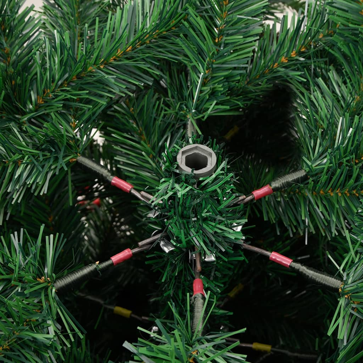 Nahaufnahme der Basis eines grünen künstlichen Weihnachtsbaums. Metallstütze mit roten und gelben Akzenten. Grüne Nadeln bedecken den Baum.