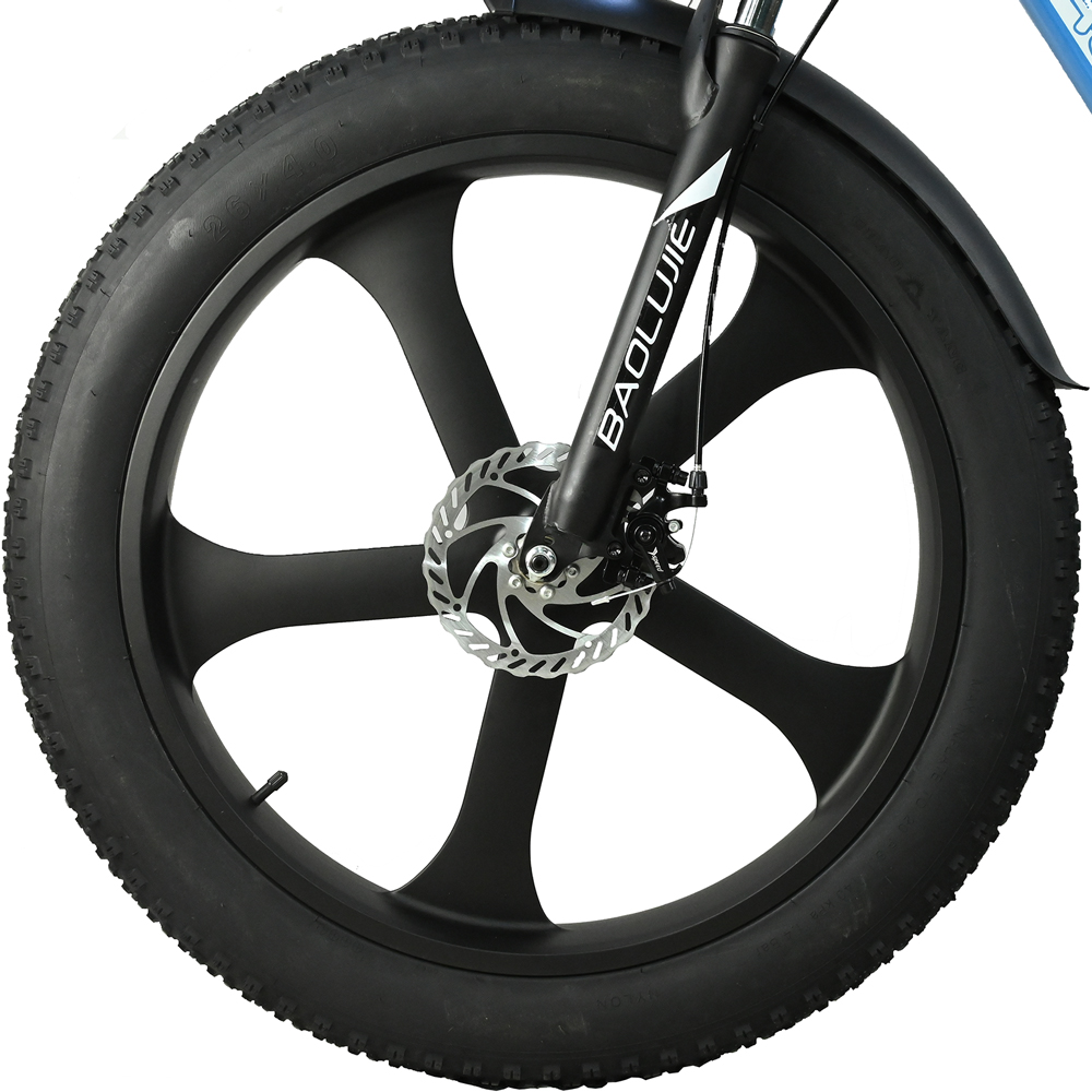 Primer plano de una rueda de bicicleta negra con freno de disco. El neumático tiene una superficie texturizada. La rueda tiene un diseño único de radios.