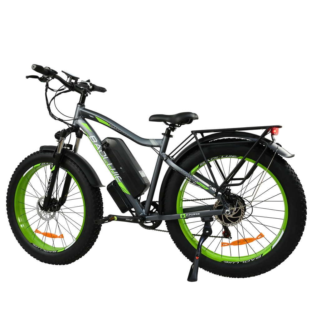 Una bicicleta eléctrica gris y negra con detalles verdes, neumáticos gruesos, una batería y un portaequipajes trasero. La bicicleta está sobre un fondo blanco.