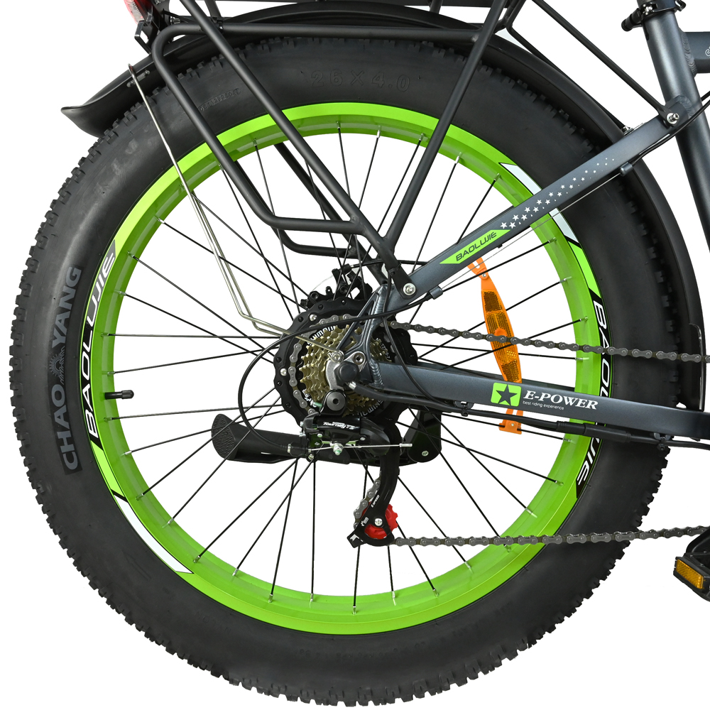 Primer plano de una rueda de bicicleta. Neumático negro con llanta verde. La bicicleta tiene un cuadro negro y un portaequipajes trasero. Visibles la cadena y los engranajes.