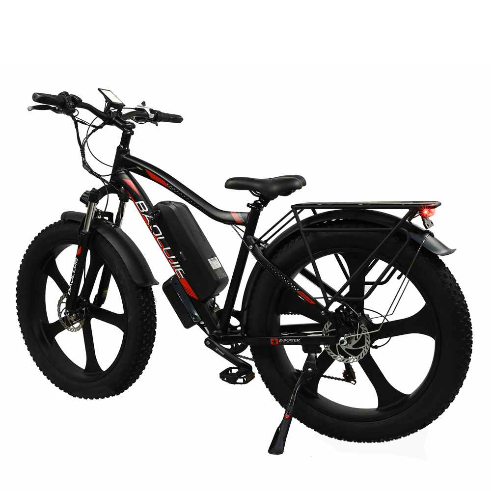 Bicicleta eléctrica negra con neumáticos gruesos. Detalles rojos en el cuadro y la batería. Portaequipajes trasero y pata de cabra visibles. Fondo blanco.