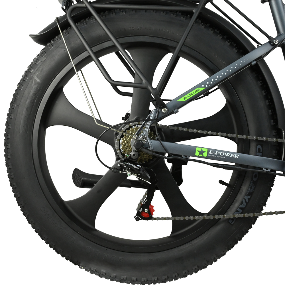 Primer plano de una rueda de bicicleta negra. El neumático es grueso, la rueda tiene un diseño único. Se ven partes del cuadro, la cadena y los engranajes.