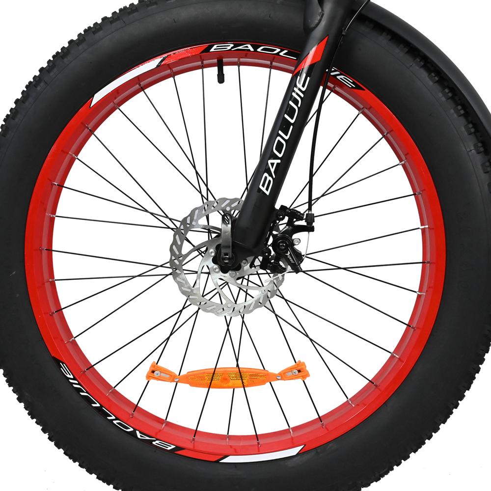Primer plano de una rueda de bicicleta. Neumático negro con llanta roja y radios. Se ven el freno de disco y el reflector naranja.