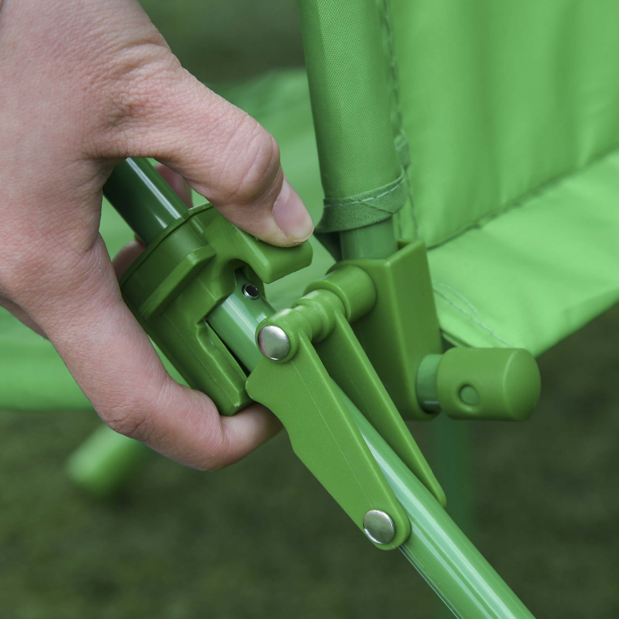 Una mano regola una sedia pieghevole verde. La sedia è su una superficie erbosa verde.