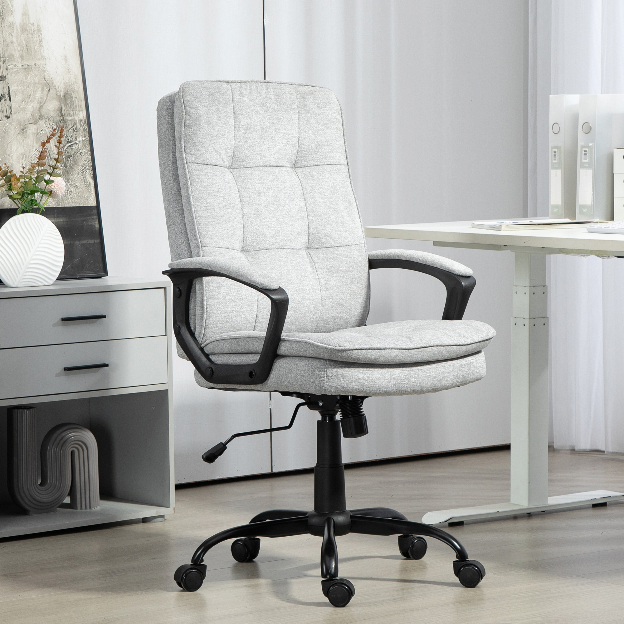 Una sedia da ufficio grigia con base e braccioli neri si trova in un ufficio. Sullo sfondo una scrivania e un armadio.