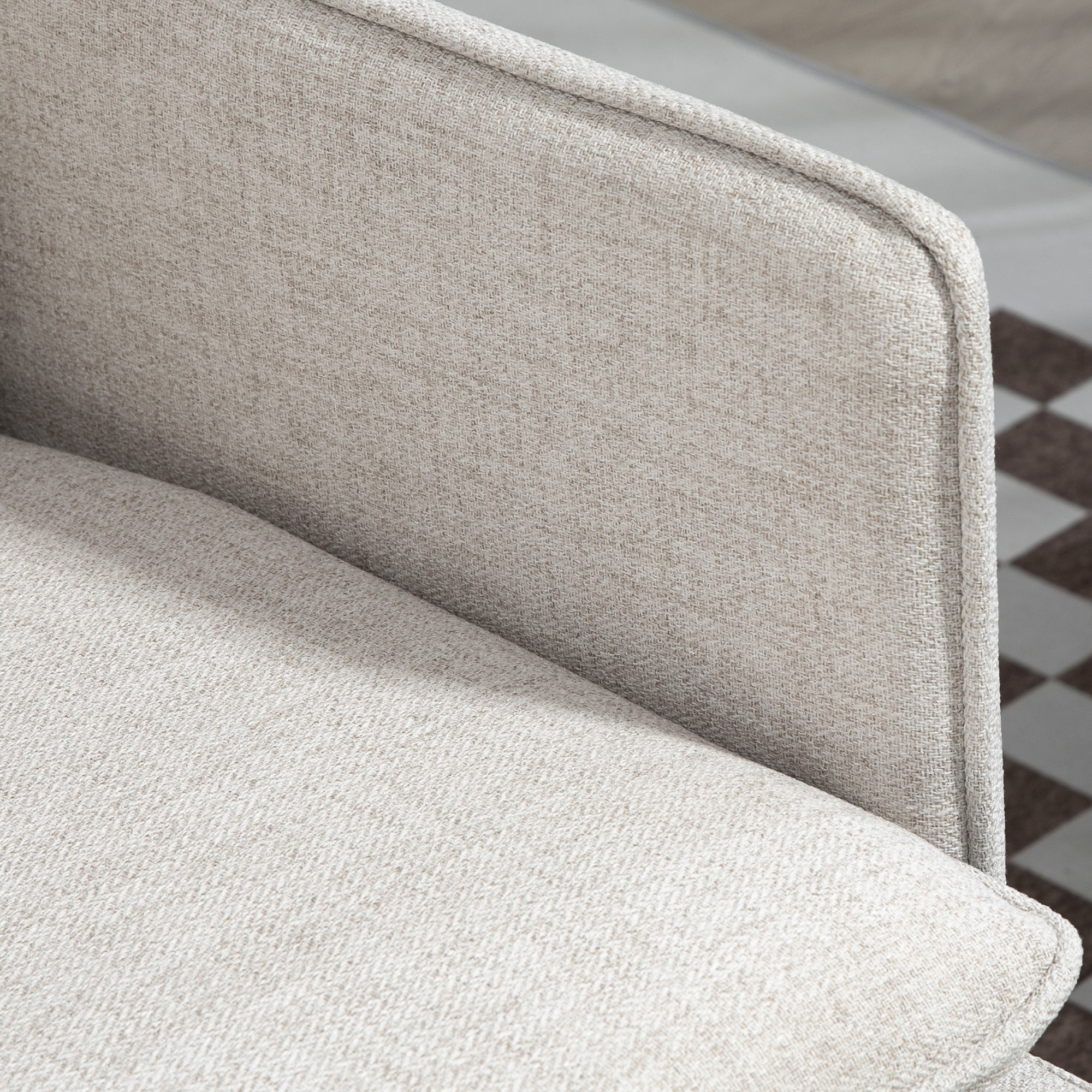 Primo piano di una poltrona imbottita beige. La trama del tessuto è visibile. Sullo sfondo si vede un pavimento a fantasia.