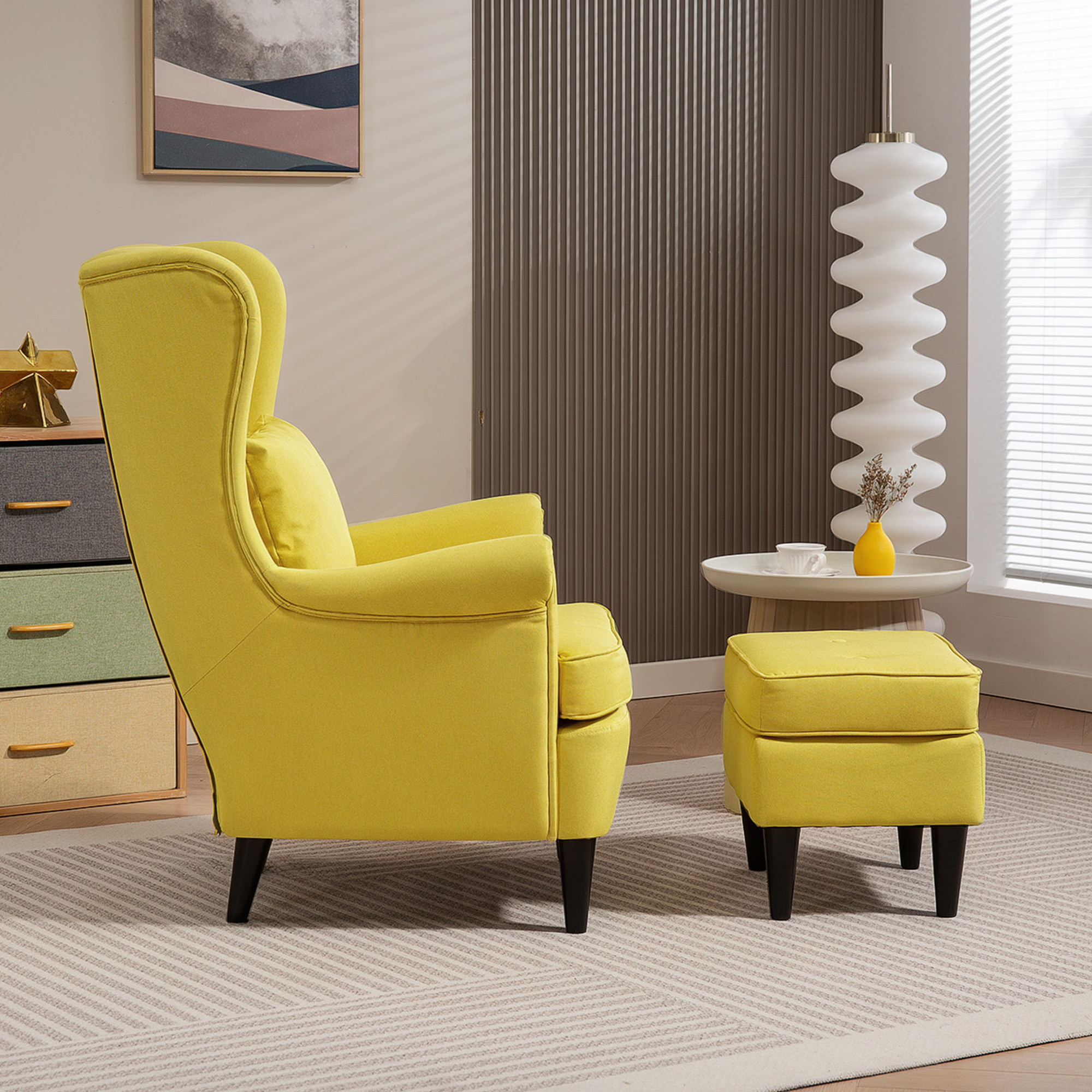 Una poltrona e un pouf gialli su un tappeto fantasia. Un tavolino bianco con un vaso giallo. Un quadro appeso alla parete.