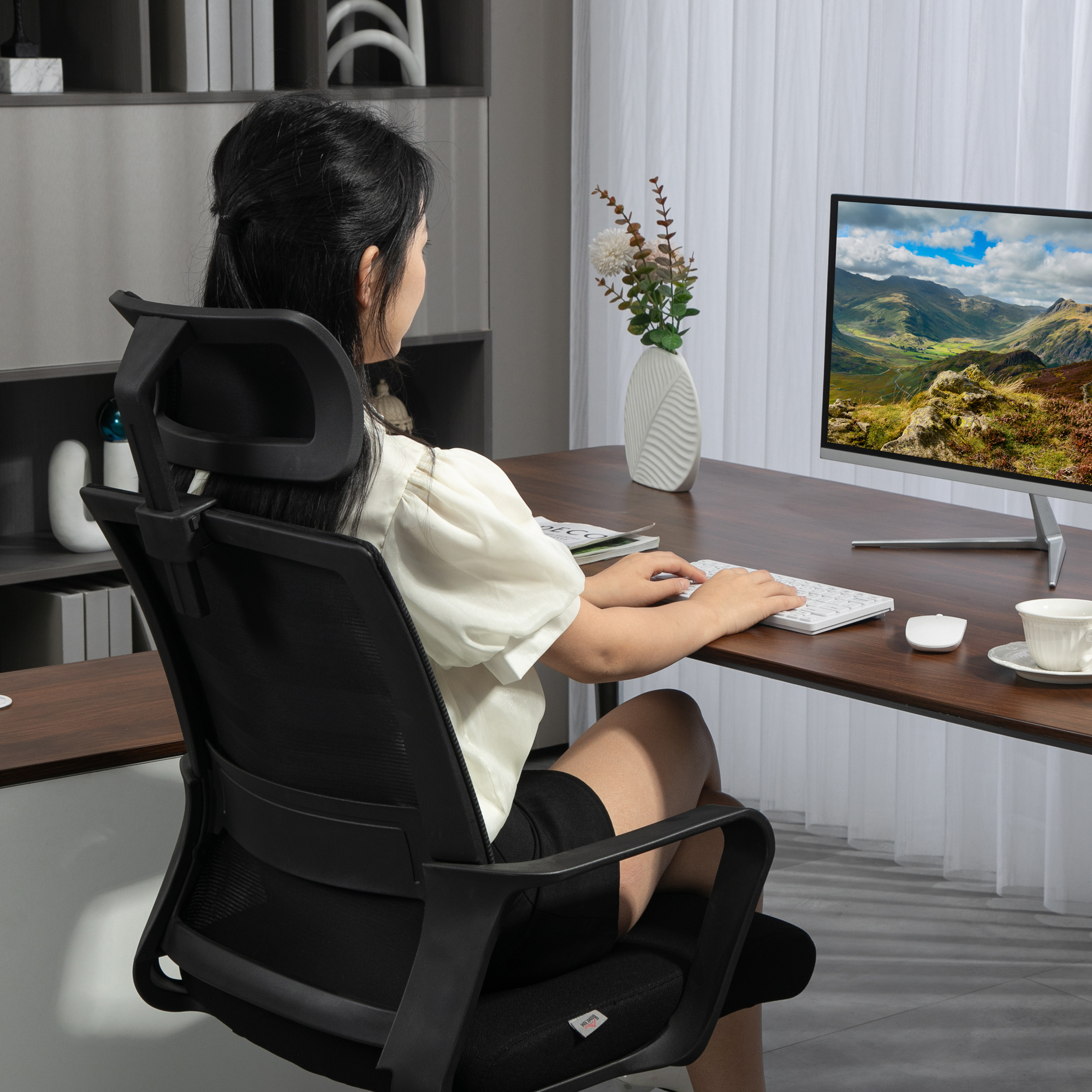 Donna alla scrivania con computer. Sta digitando sulla tastiera. Un paesaggio montano è sul monitor.