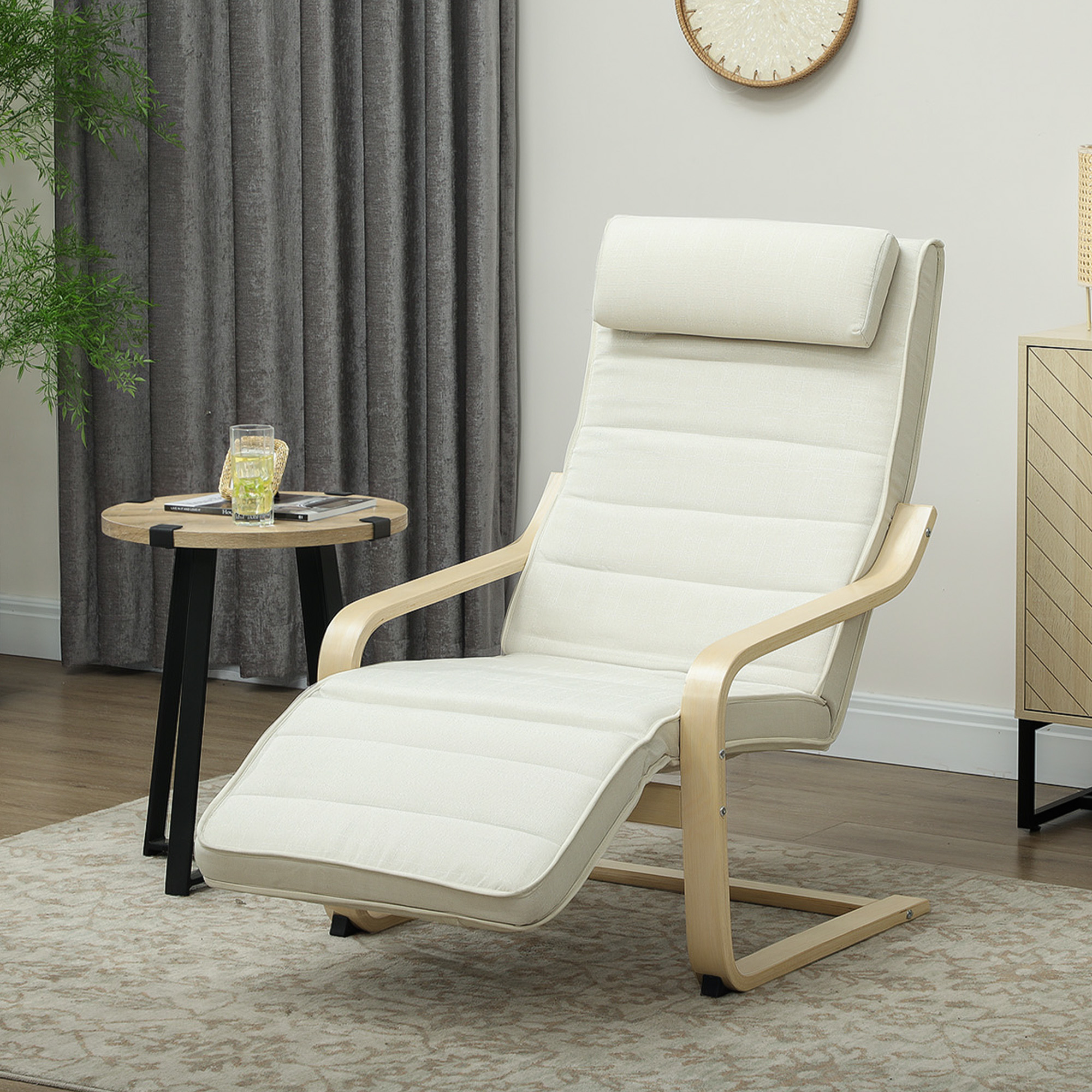Una poltrona reclinabile color crema con struttura in legno chiaro. Sono presenti anche un tavolino, un bicchiere d'acqua e tende grigie.