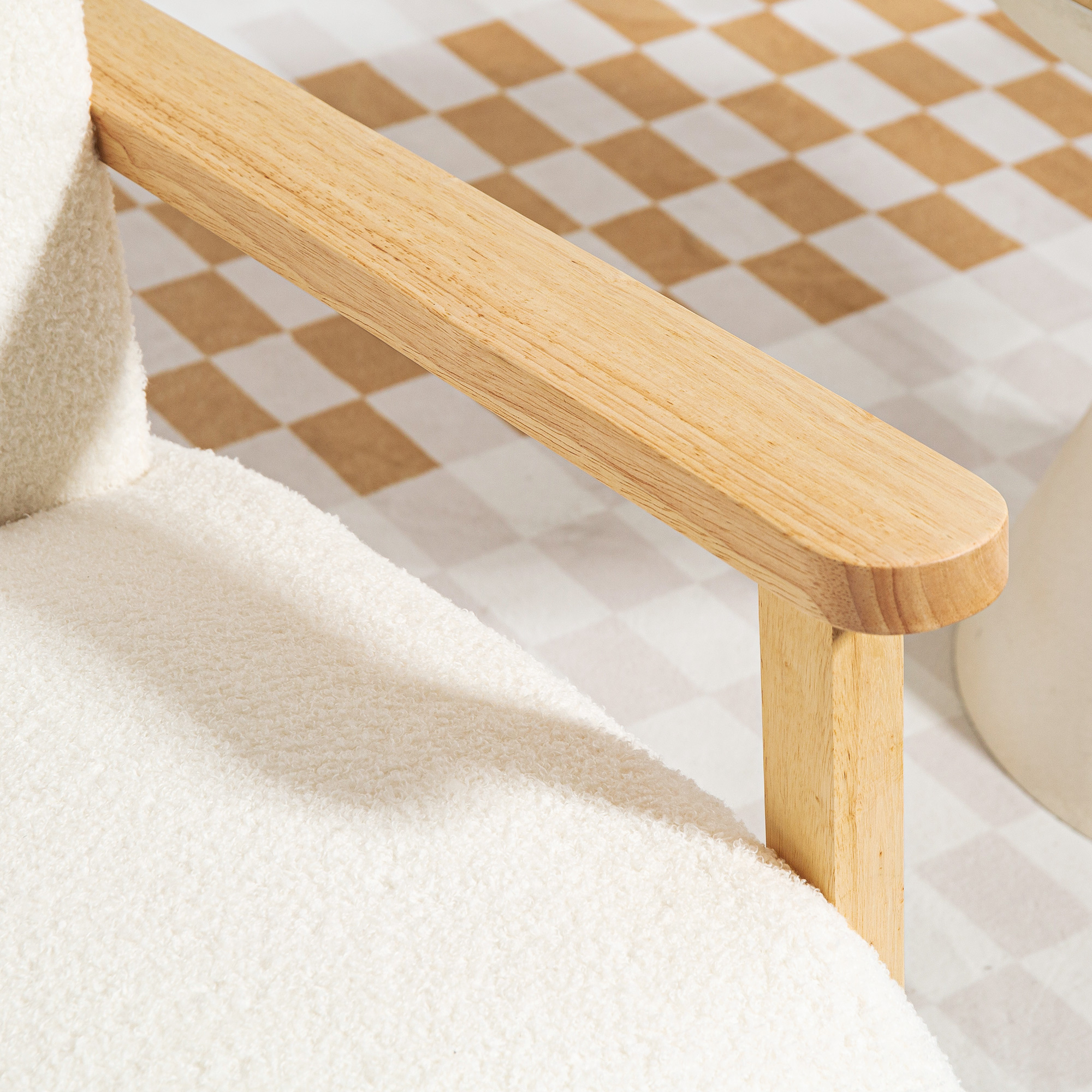 Primo piano di un bracciolo bianco e soffice e di un braccio di legno con sfondo a quadri beige e bianco.