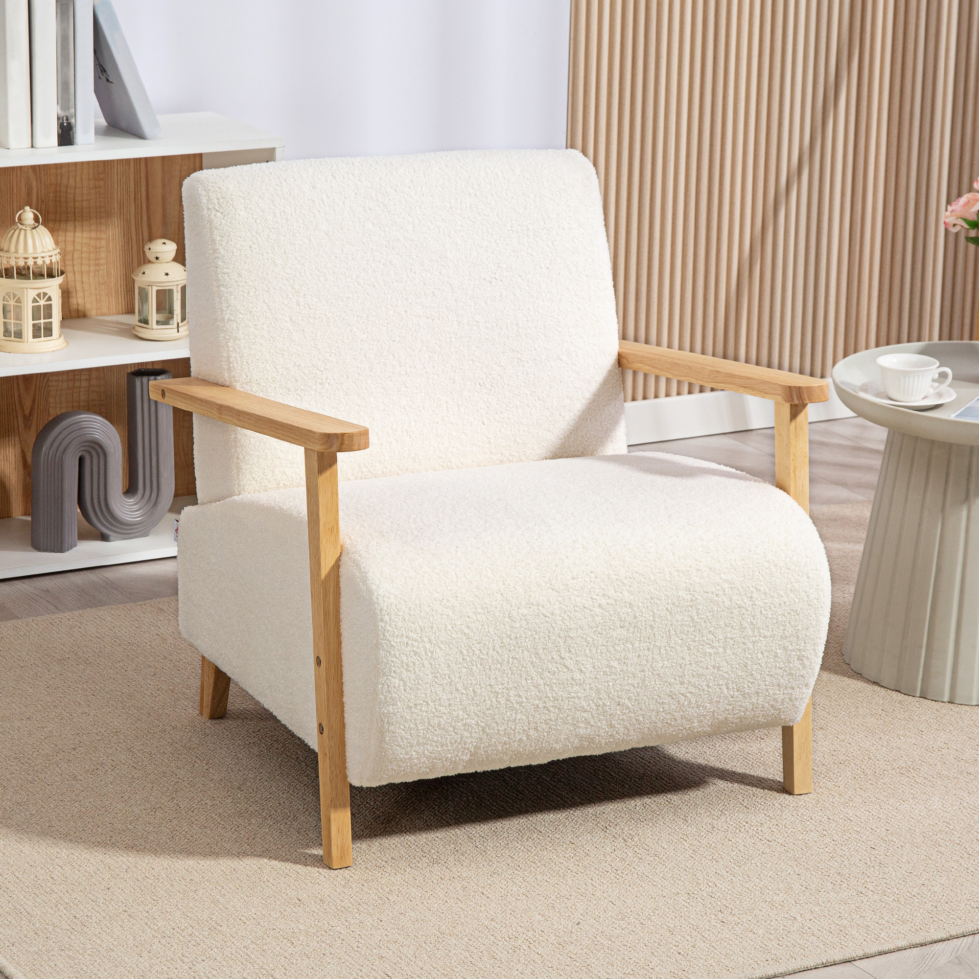 Una poltrona bianca e soffice con braccioli in legno è su un tappeto beige. Un tavolino con una tazza e una libreria sono sullo sfondo.