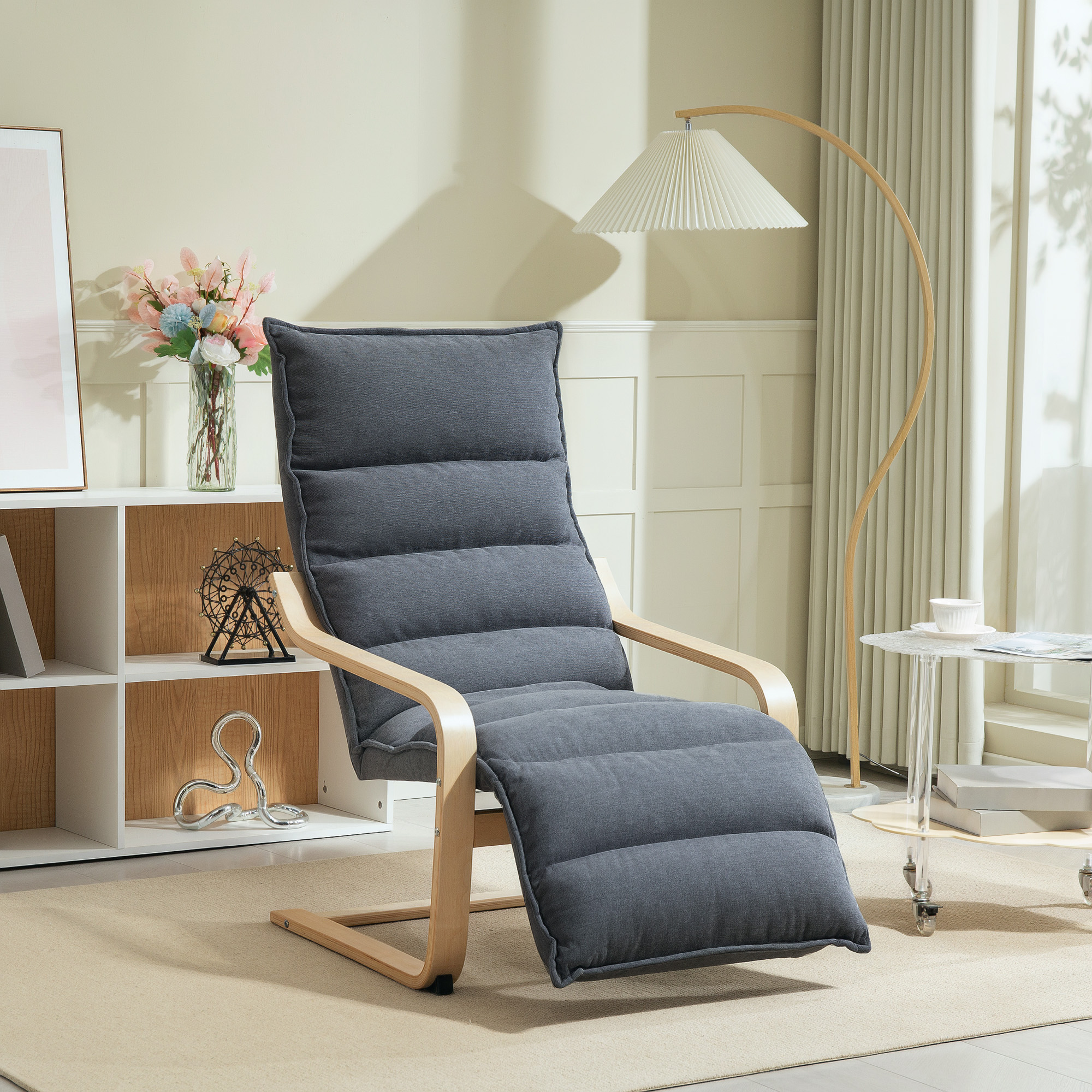 Una sedia grigia reclinabile con struttura in legno è su un tappeto beige. Una lampada e un tavolino sono accanto alla sedia.