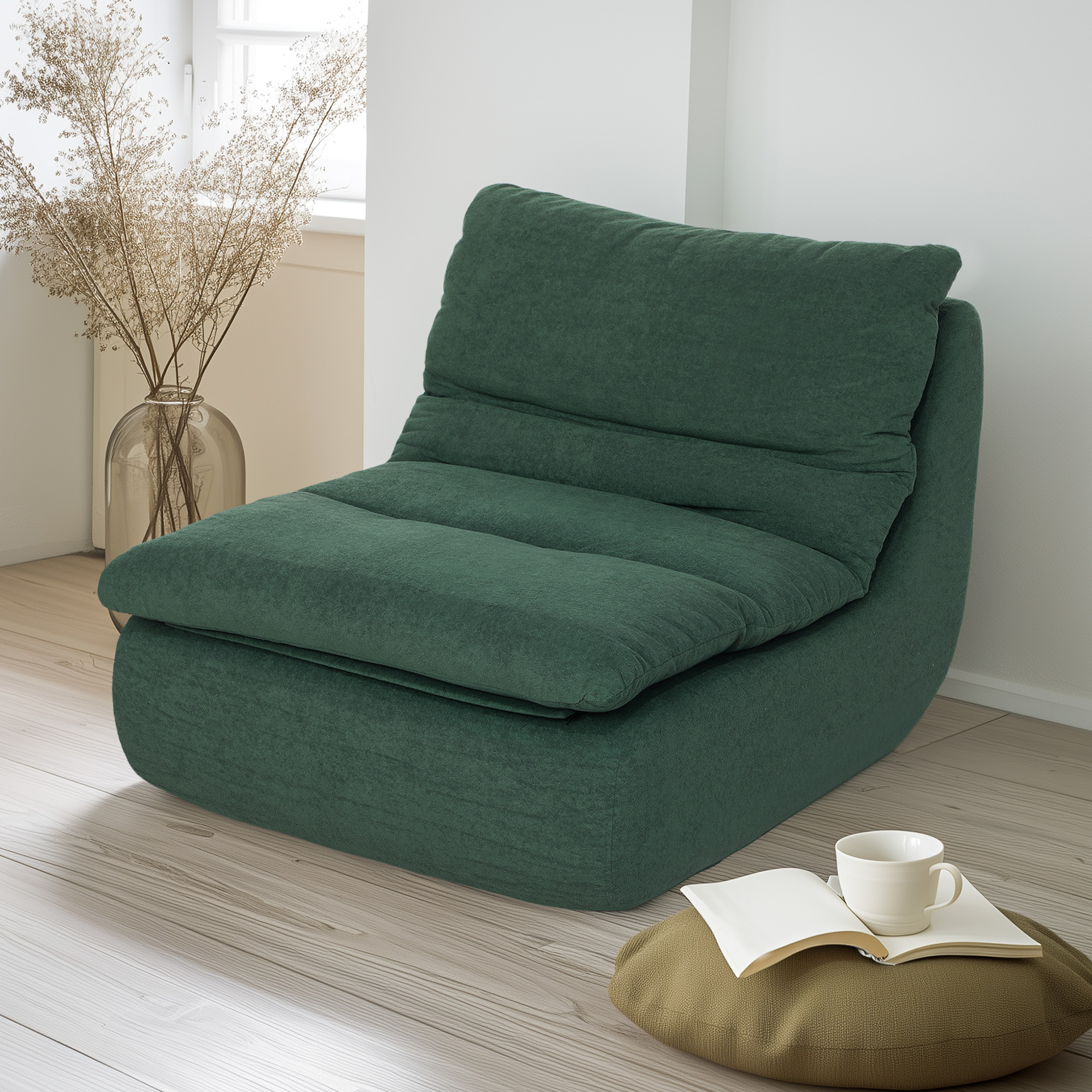 Una sedia verde scuro vicino a una finestra. Un libro e una tazza su un cuscino sul pavimento.