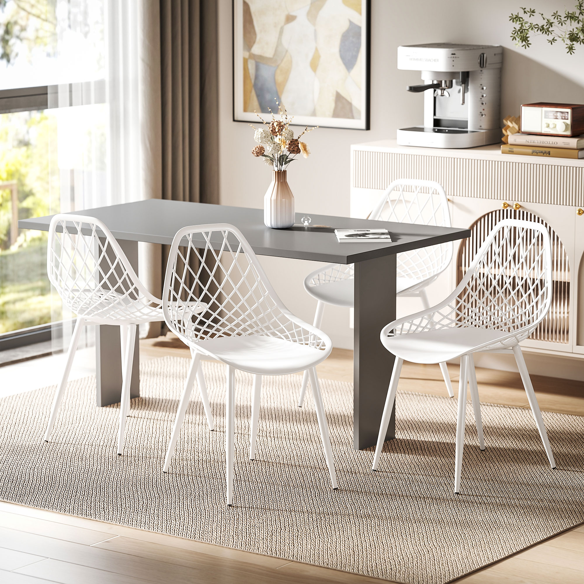 Sala da pranzo con tavolo grigio, quattro sedie bianche, fiori e macchina da caffè su un mobile.