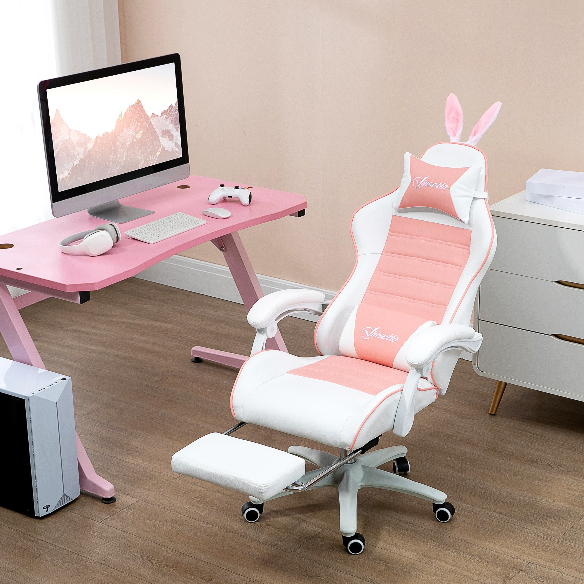 Una scrivania rosa con monitor, cuffie, tastiera e una sedia da gioco con orecchie da coniglio. Un armadio bianco a destra.