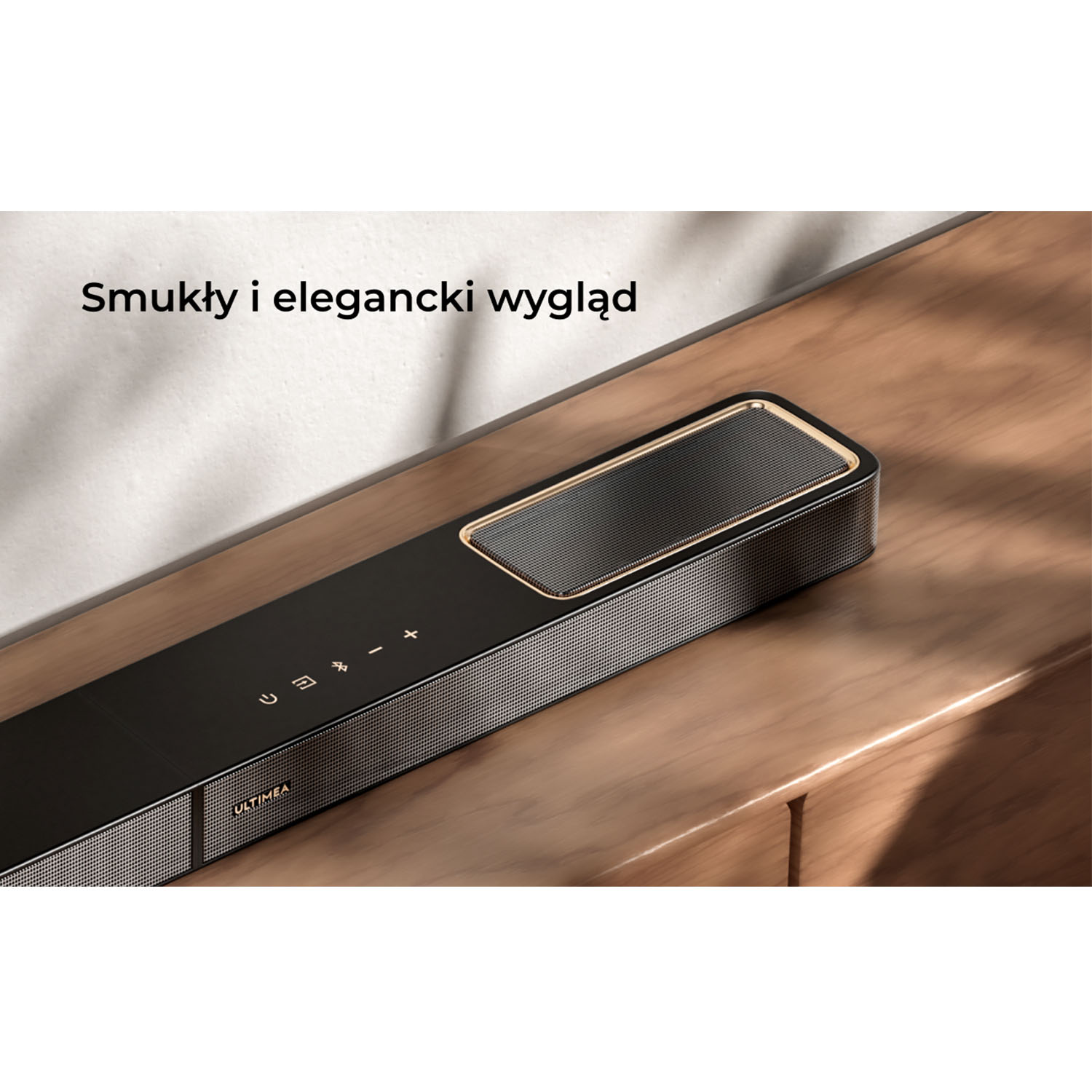 Czarny soundbar z siatkową kratką leży na drewnianej powierzchni. Posiada przyciski sterowania i markę ULTIMEA.
