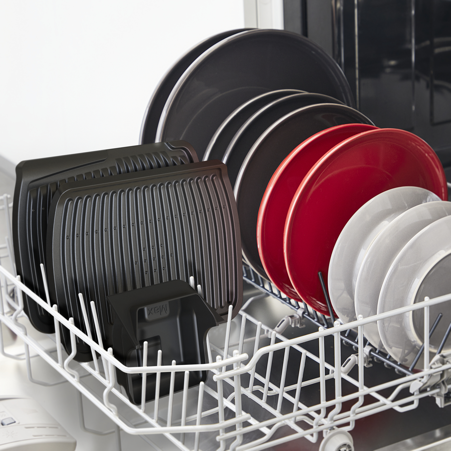 Zmywarka załadowana talerzami w różnych kolorach. Widoczne również tacki do grillowania i mały pojemnik.
