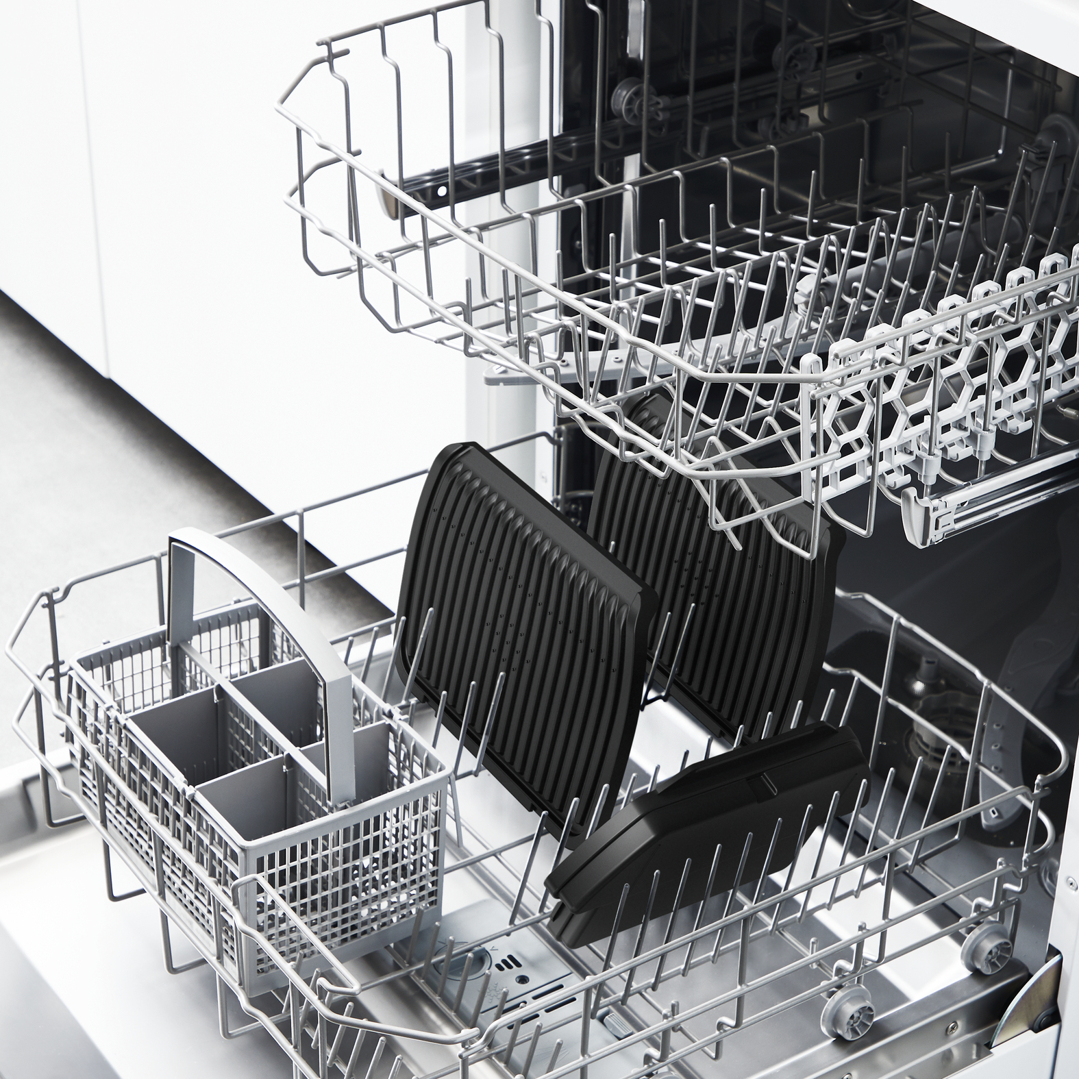 Zmywarka z czarnymi patelniami do grillowania i koszem na sztućce. Zmywarka jest otwarta i gotowa do załadunku.