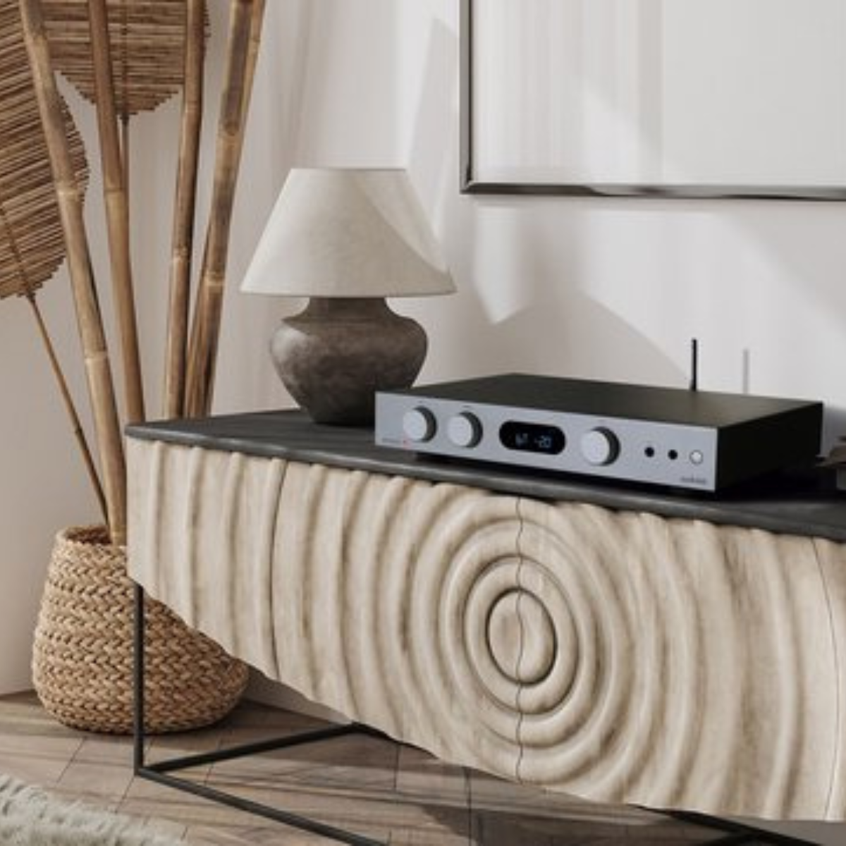 A black and silver audio amplifier on a wooden cabinet. A lamp and bamboo sticks are next to it. A woven basket is on the left.
