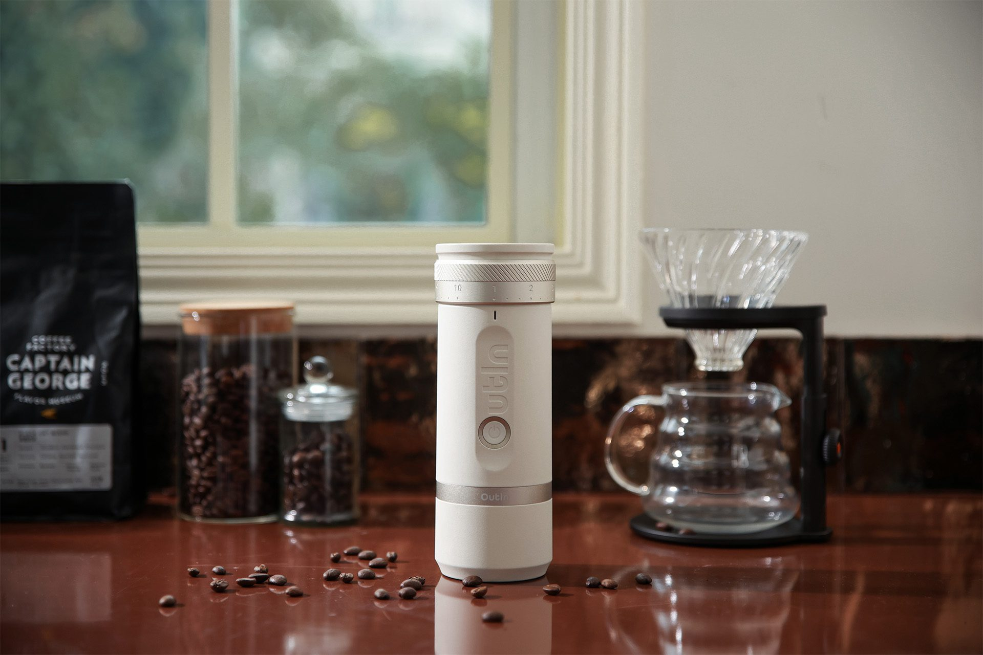 Biały młynek do kawy, ziarna kawy i ekspres do kawy na drewnianej powierzchni, przy oknie.