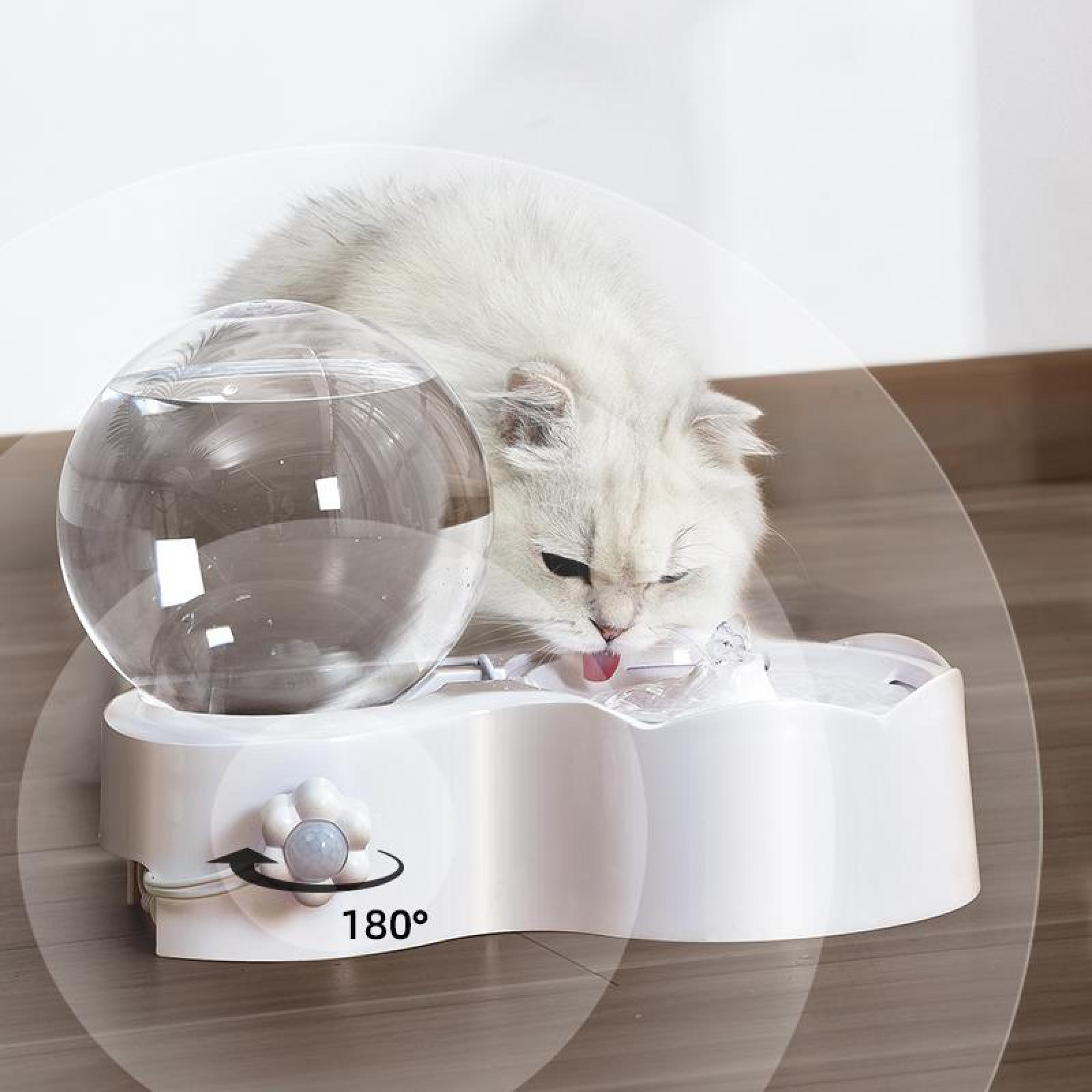 Eine weiße Katze trinkt Wasser aus einem weißen Wasserbrunnen. Oben befindet sich eine klare Wasserkugel. Die Zunge der Katze ist sichtbar.