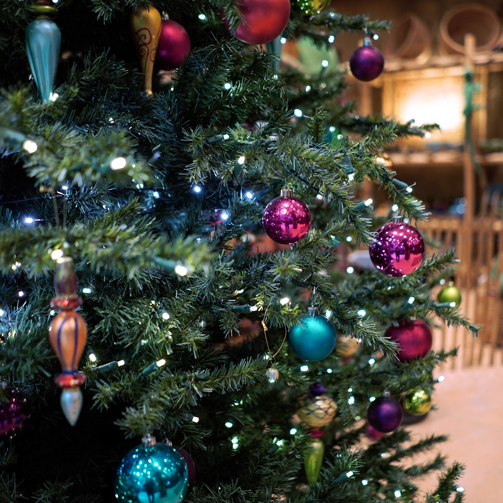 Weihnachtsbaum mit bunten Ornamenten und weißen Lichtern. Verschiedene Kugeln in Rot, Lila und Blaugrün sind sichtbar.