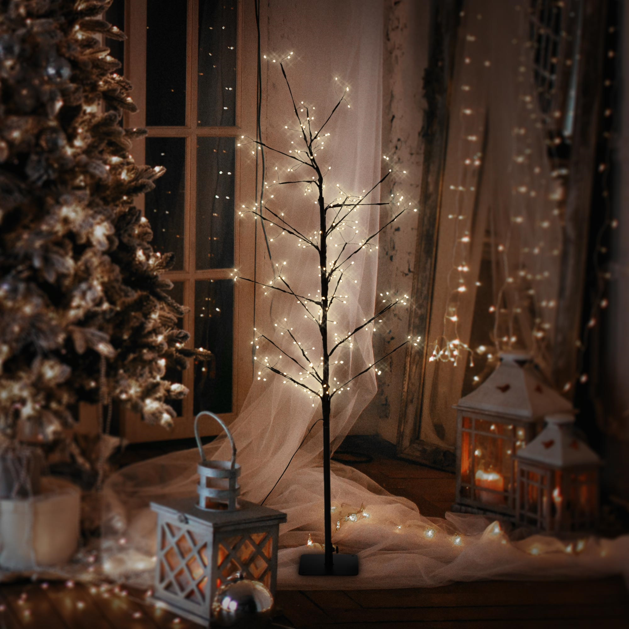 Ein dekorativer Baum mit Lichtern, zwei Laternen und einem Weihnachtsbaum, der eine warme, festliche Atmosphäre schafft.