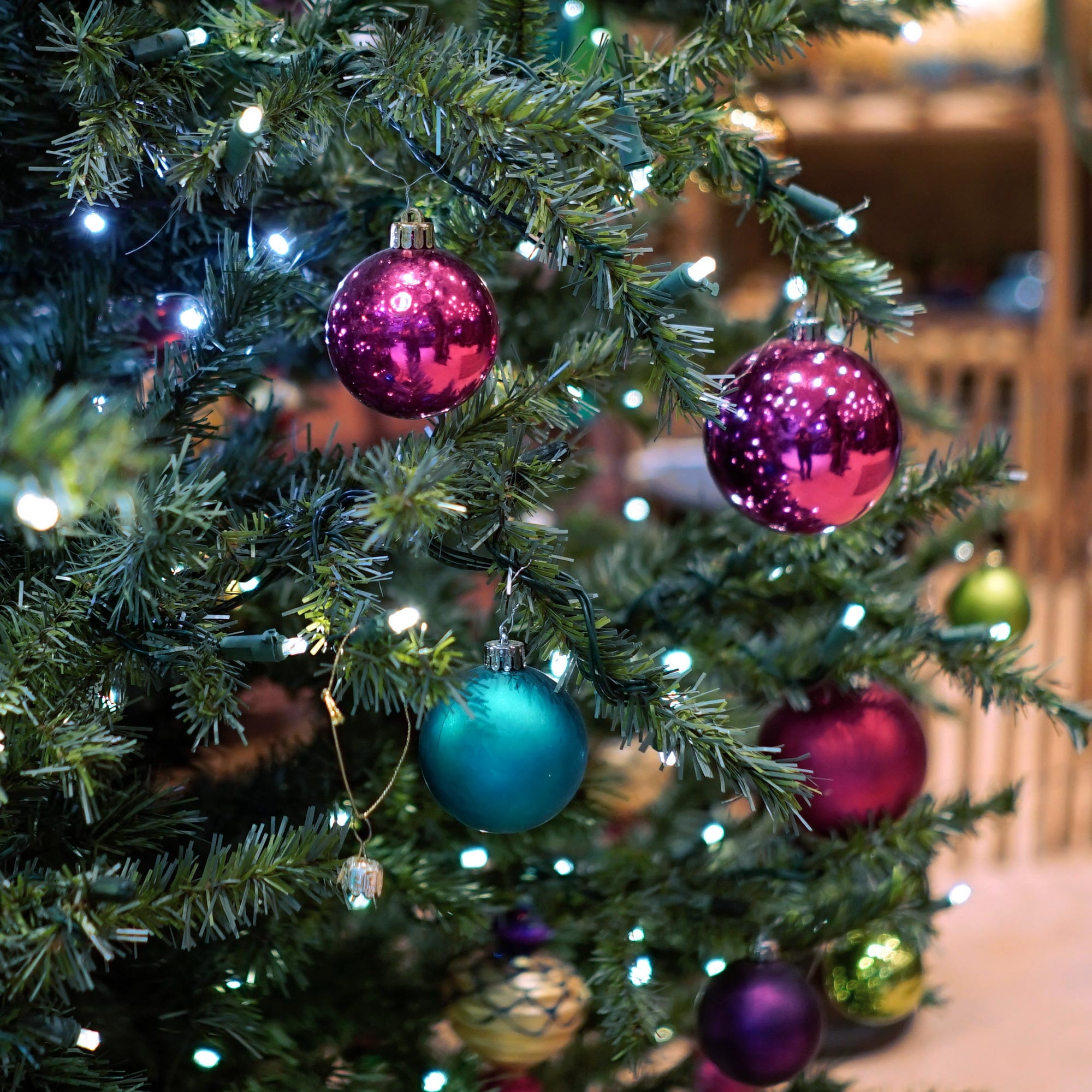 Ein Weihnachtsbaum mit Ornamenten. Mehrere bunte Kugeln und weiße Lichter an den Ästen. Der Hintergrund ist unscharf.