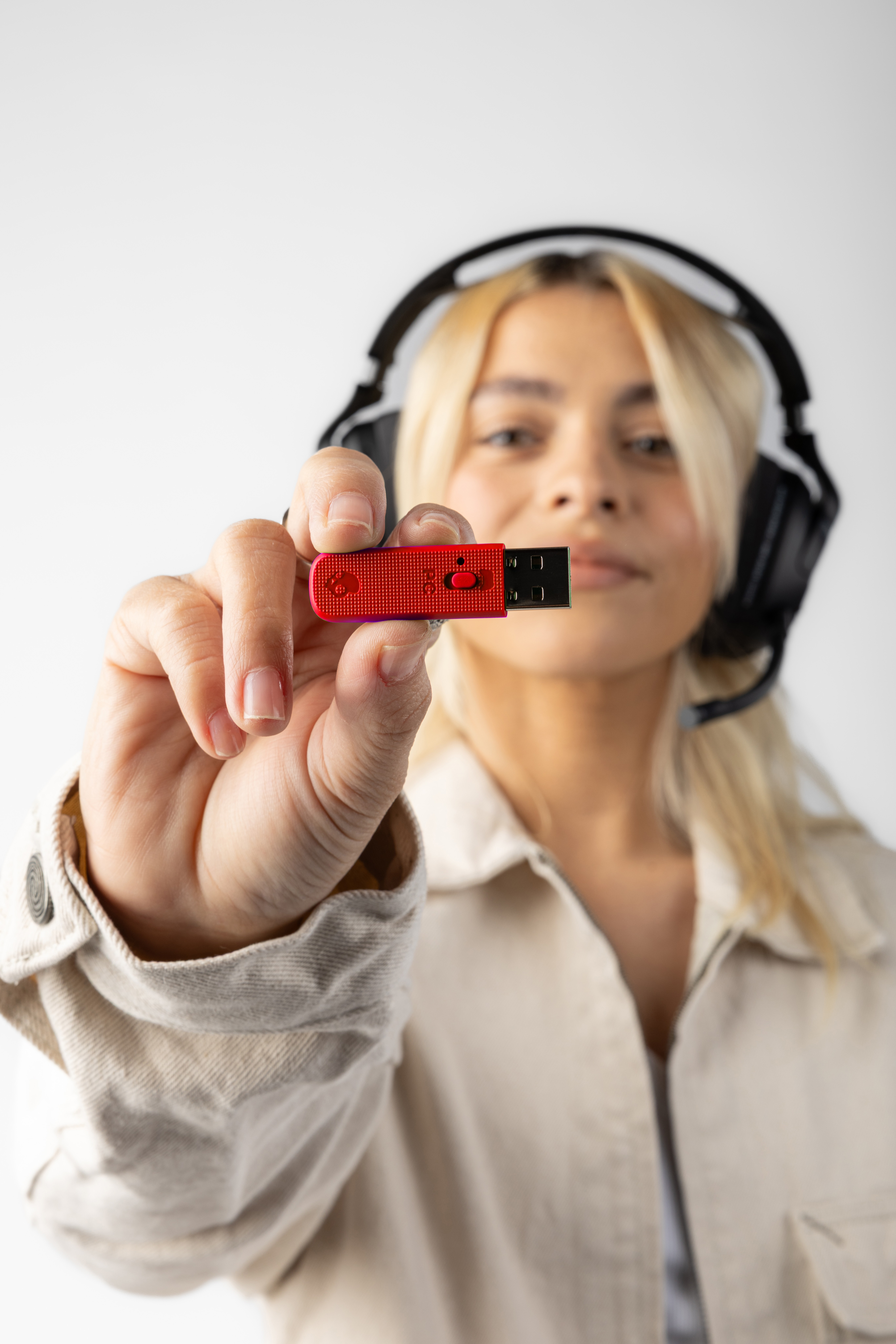 Kobieta trzyma czerwoną pamięć USB. Ma słuchawki i beżową kurtkę, z białym tłem.