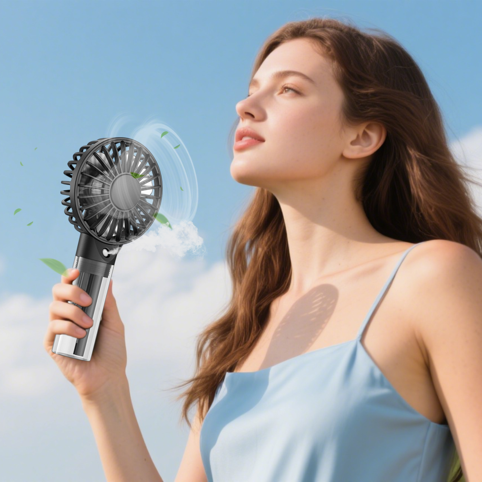 Eine Frau hält einen tragbaren Ventilator und blickt in den Himmel. Der Ventilator bläst Nebel und Blätter. Sie trägt ein blaues Kleid.