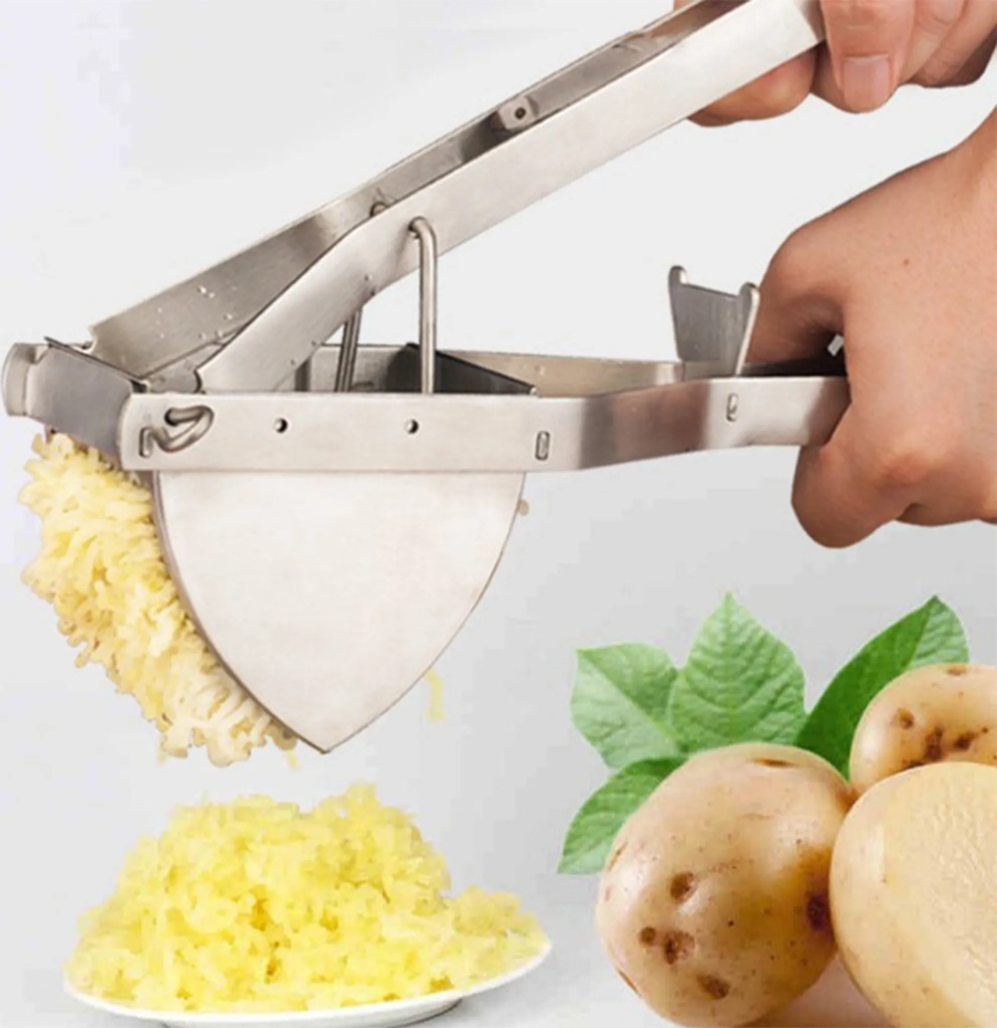Eine Kartoffelpresse aus Metall wird benutzt. Gelbe, zerkleinerte Kartoffeln werden gepresst. Kartoffeln und Blätter sind im Hintergrund.