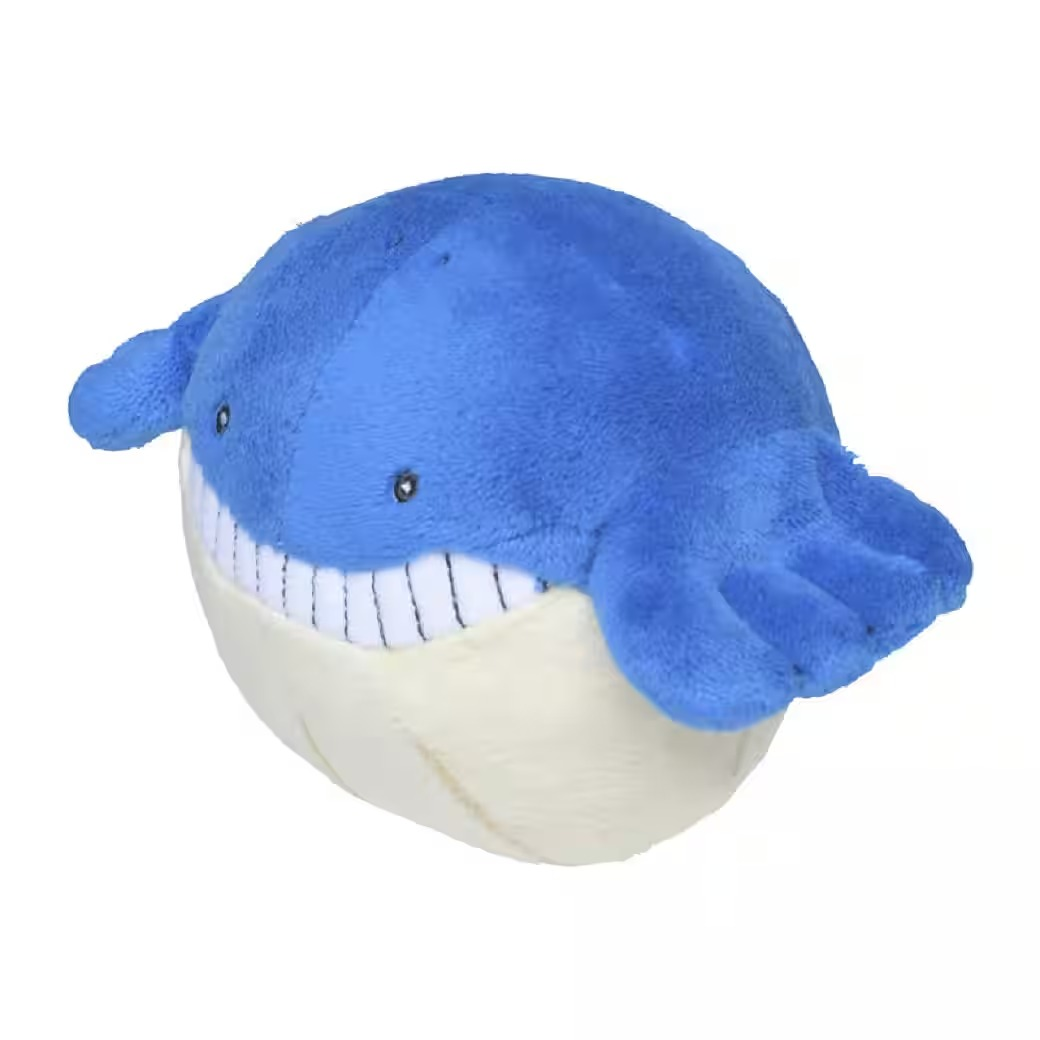 Ein Plüschtier eines blauwalartigen Wesens mit lächelndem Gesicht und weißen Zähnen. Der Unterkörper ist beige.