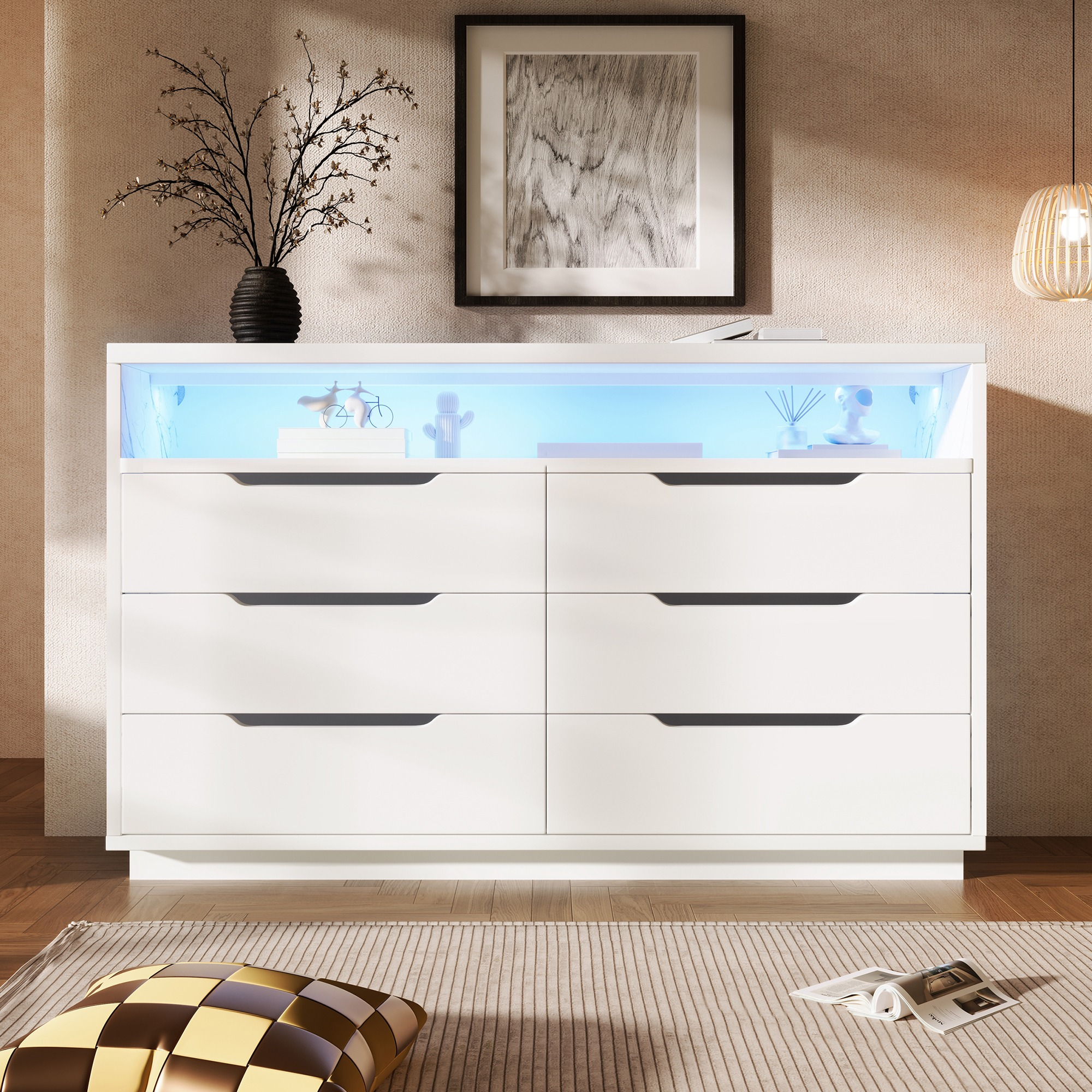 Eine weiße Kommode mit sechs Schubladen, beleuchtetes Innenregal. Objekte auf dem Regal, Bild an der Wand, Kissen und Teppich auf dem Boden.