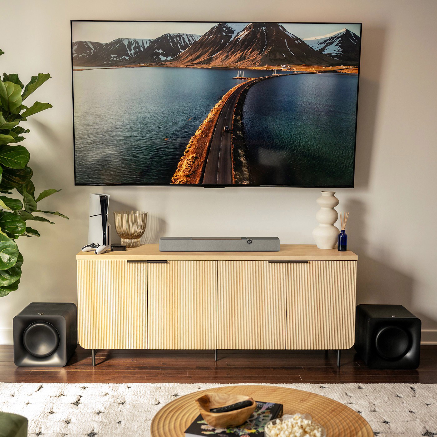 Un salotto con una grande TV che mostra un ponte sull'acqua, un mobile in legno, altoparlanti e oggetti decorativi.
