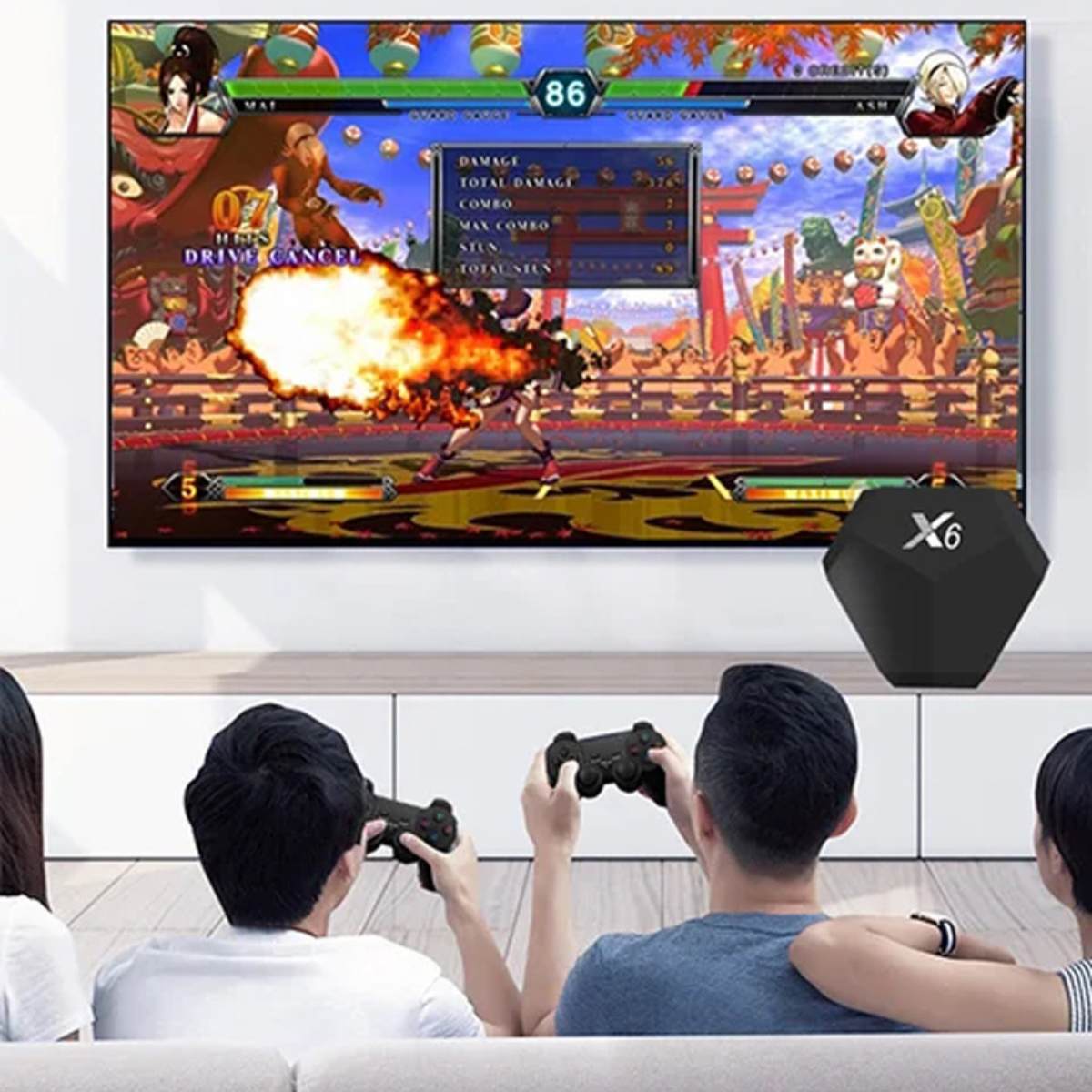 Leute spielen ein Kampfspiel auf einem Fernseher. Rechts ist eine schwarze Konsole. Spieler halten Controller und sitzen auf einem Sofa.