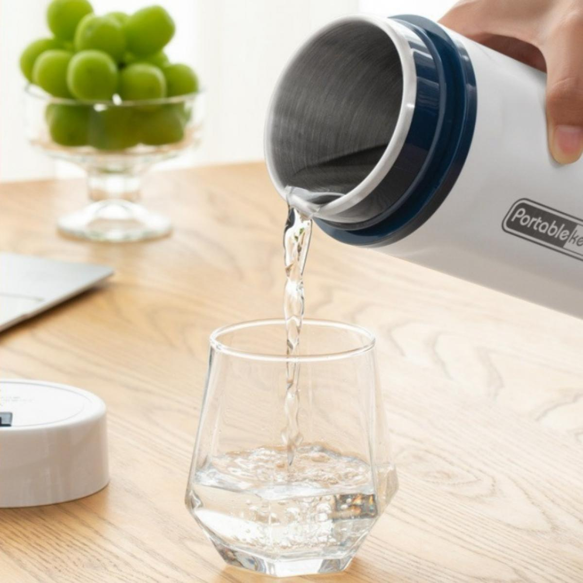 Wasser wird aus einer weißen Thermoskanne in ein Glas gegossen. Grüne Trauben in einer Glasschale stehen auf dem Tisch. Ein Laptop ist ebenfalls zu sehen.